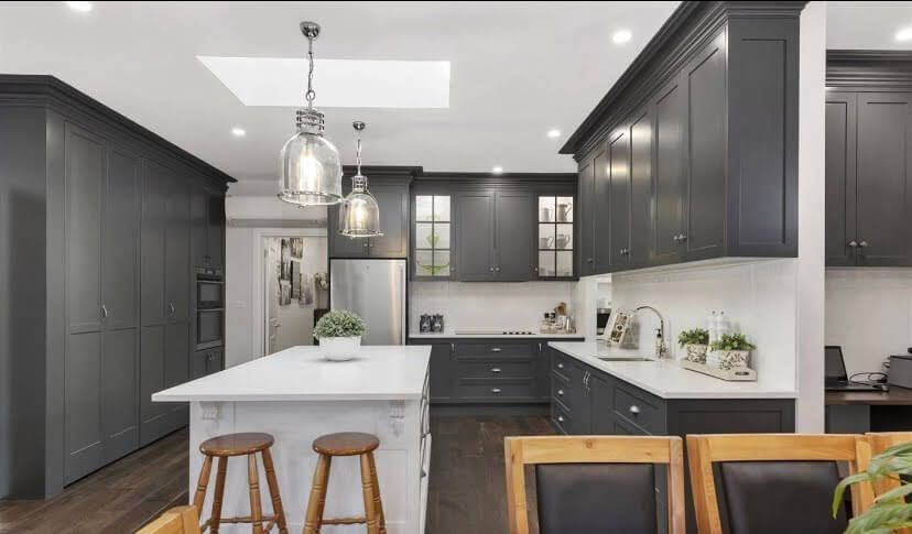 A kitchen with gray cabinets , white counter tops , stools and a large island.