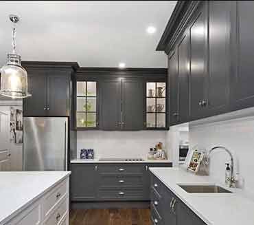 A kitchen with gray cabinets , white counter tops , stainless steel appliances and a sink.