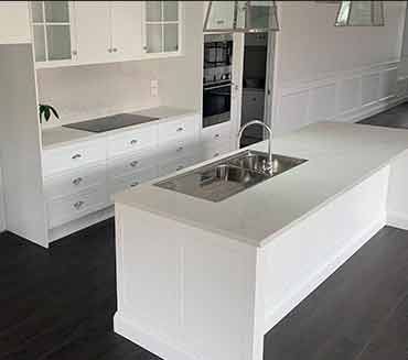 A kitchen with white cabinets and a large island with a sink.
