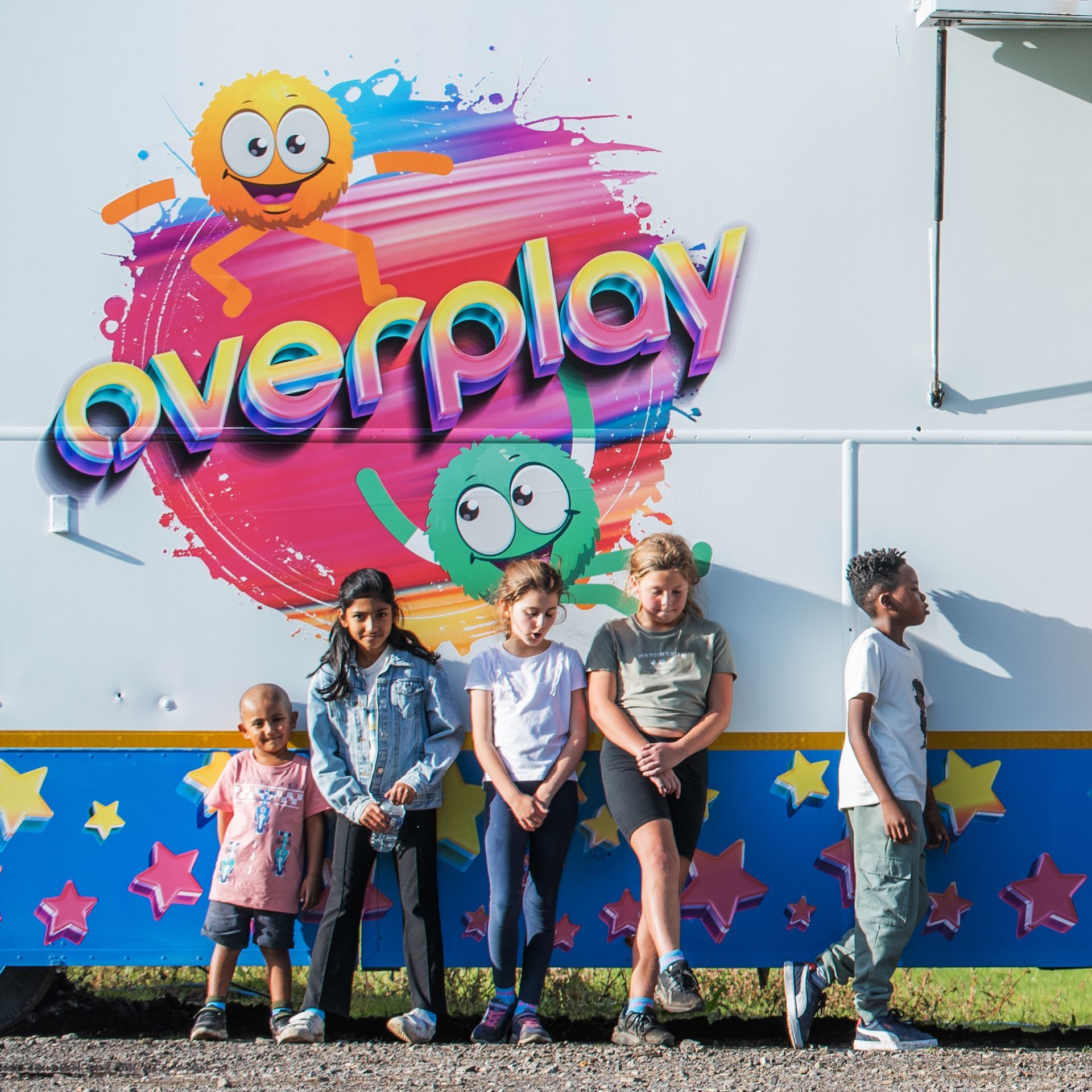 A group of children are standing in front of an overplay sign