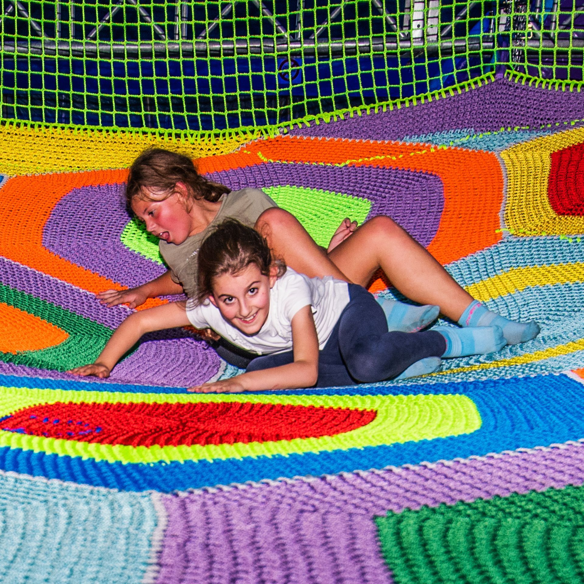 Two young girls are laying on a colorful blanket.