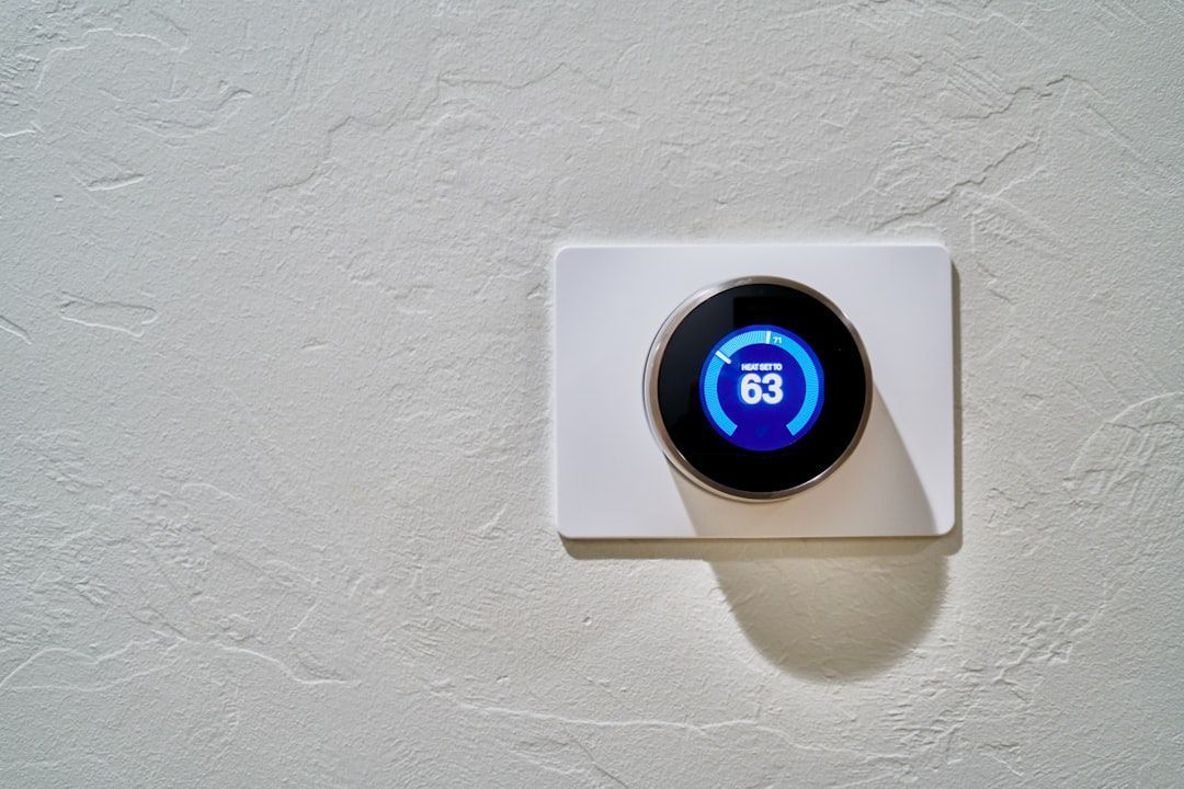 A circular smart thermostat with a blue digital display showing the number 63, mounted on a textured white wall.