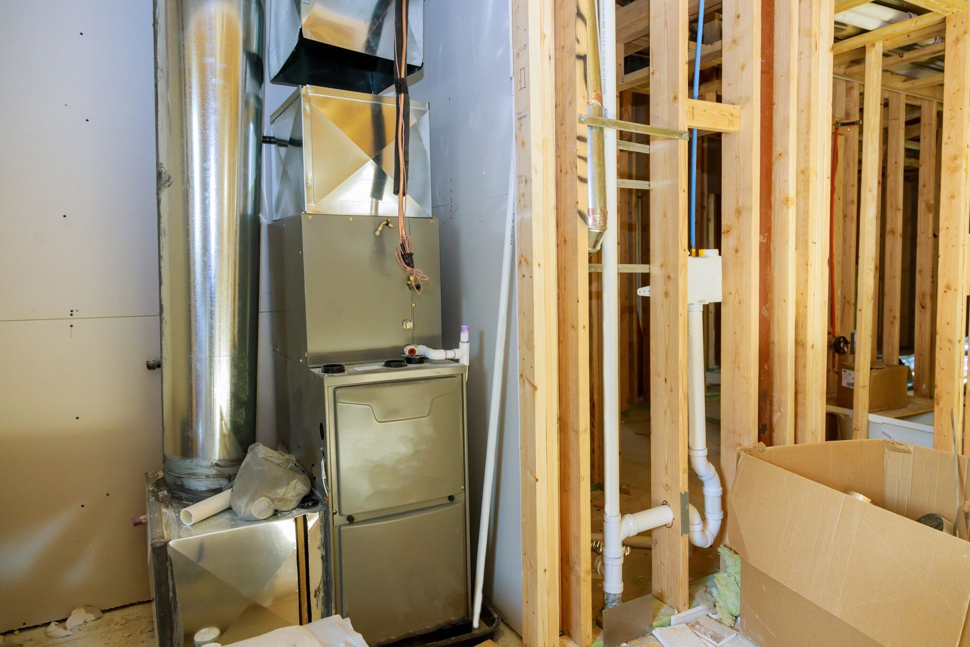 A residential furnace system in an unfinished basement with exposed wooden studs, ductwork, and PVC piping.