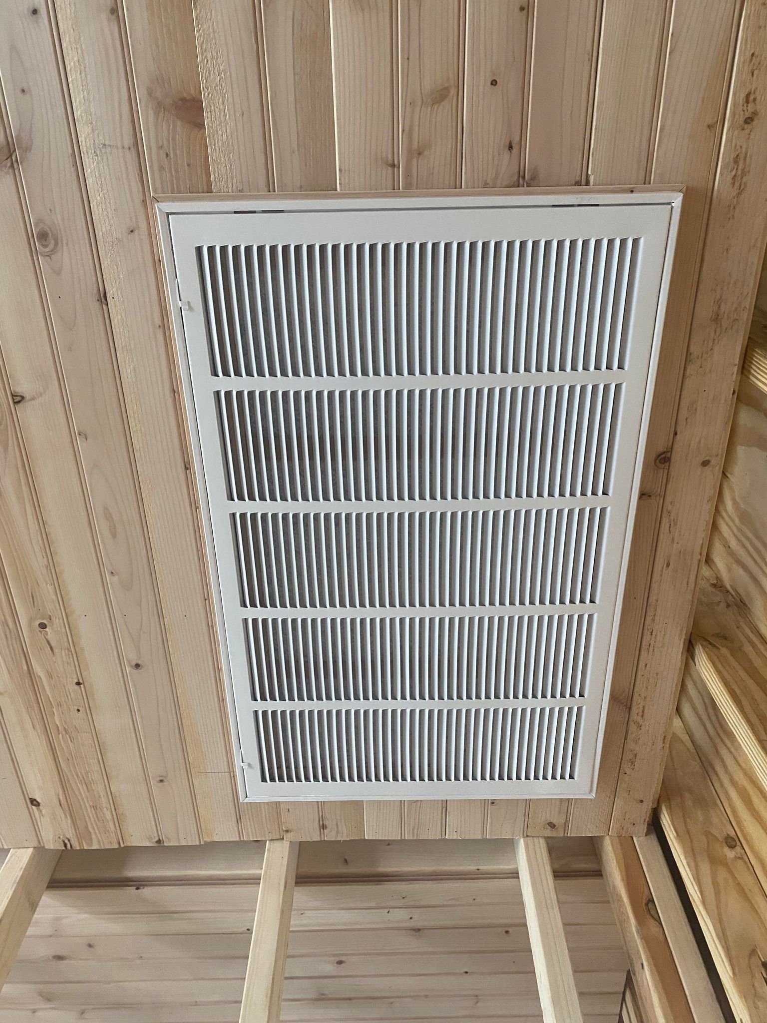 A white rectangular HVAC return air grille mounted in a light-colored wooden slat ceiling.