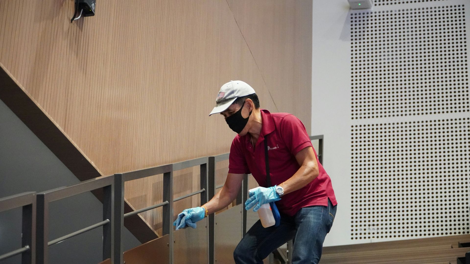 A man wearing a mask and gloves is cleaning a railing on a staircase.