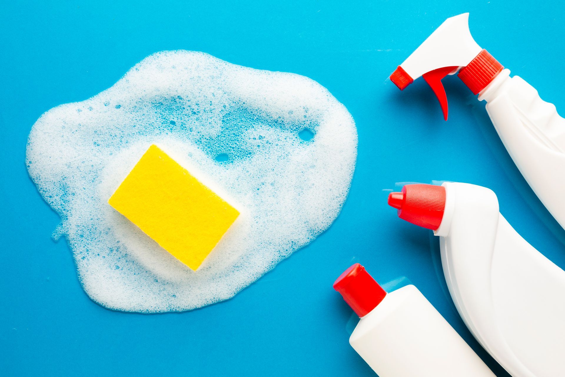 A yellow sponge is sitting on top of a pile of foam next to spray bottles.