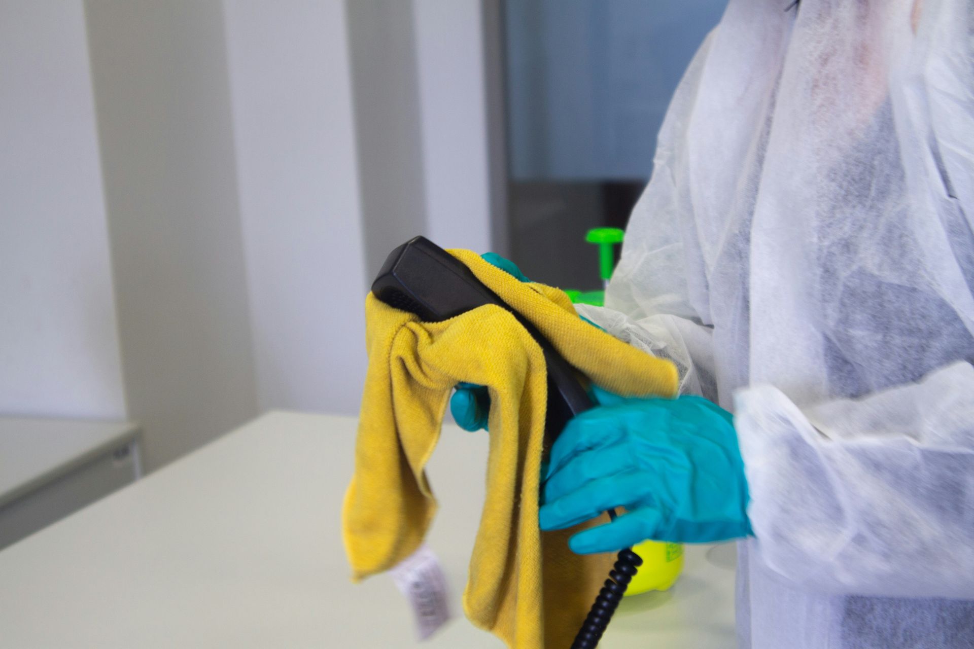 A person wearing blue gloves is cleaning a table with a yellow towel.