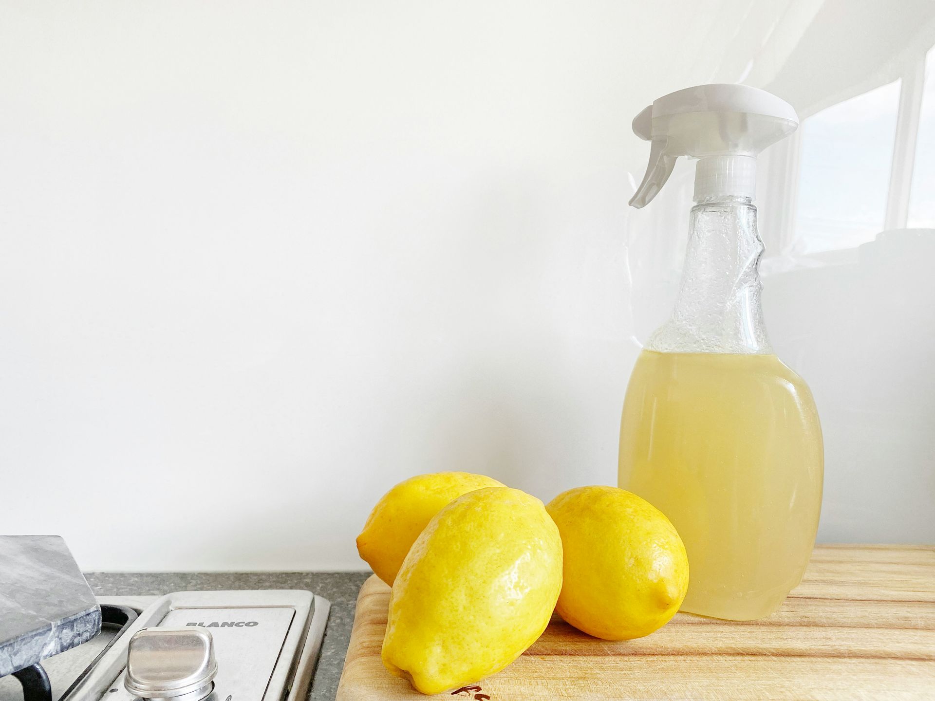 Lemons and a spray bottle on a wooden cutting board.
