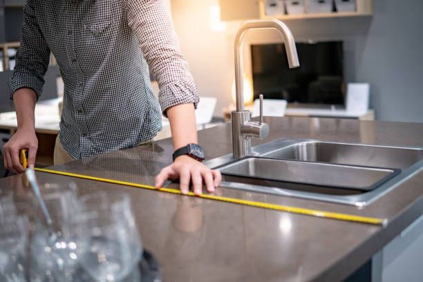 Person measuring kitchen countertop near sink in modern home interior with tape measure.
