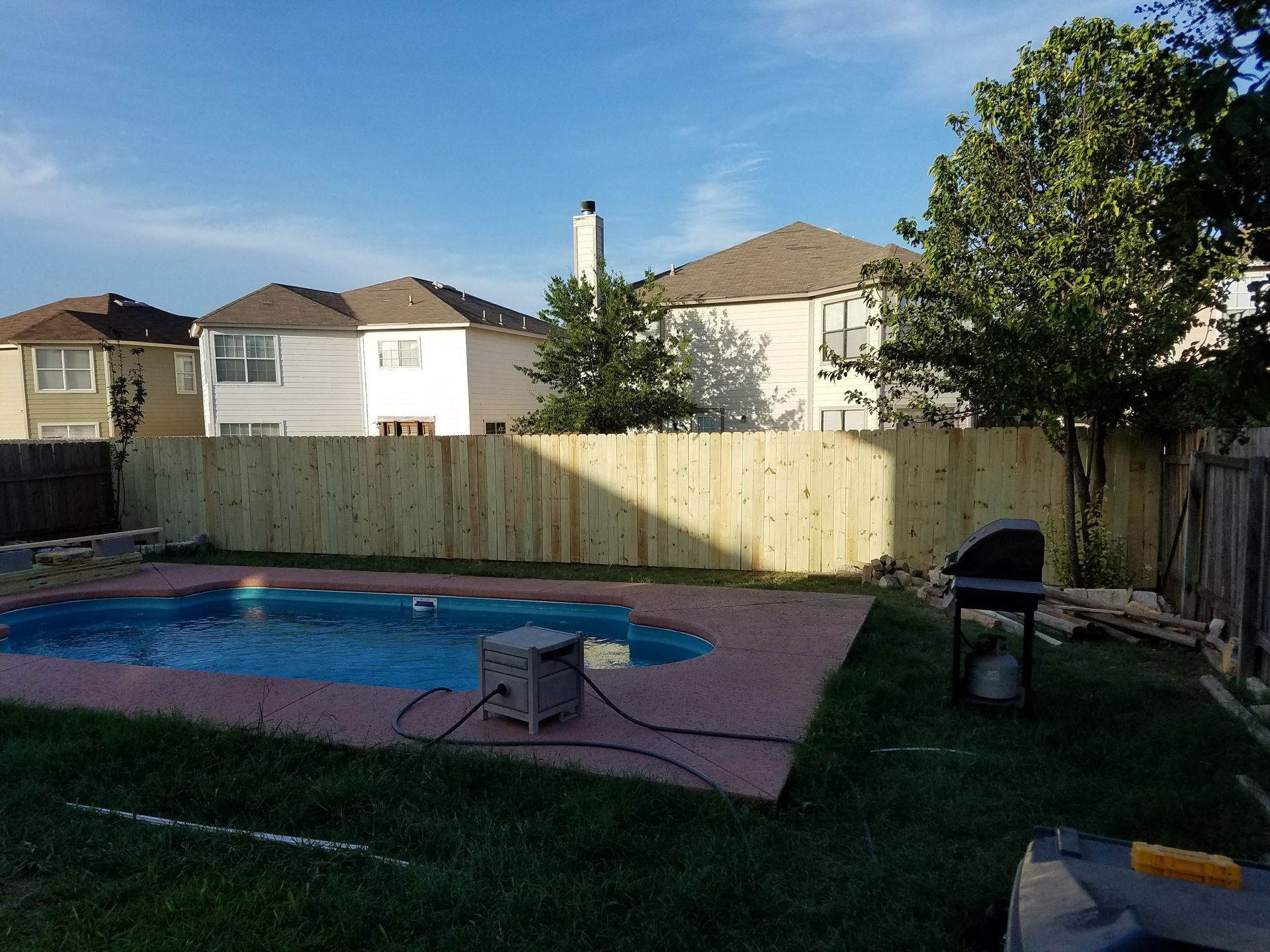 A wooden fence surrounds a swimming pool in a backyard.