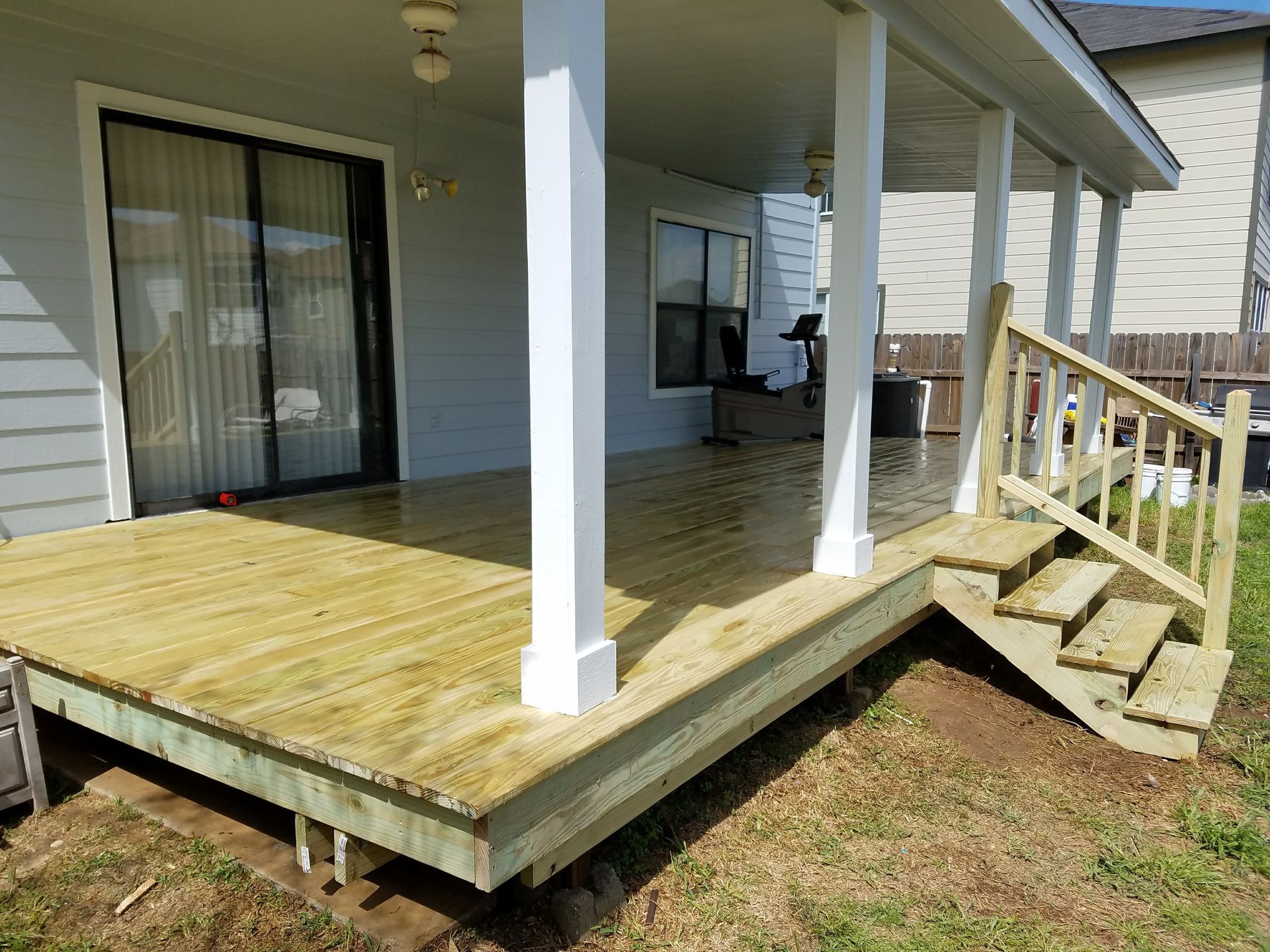 A wooden deck with stairs leading up to it is in the backyard of a house.