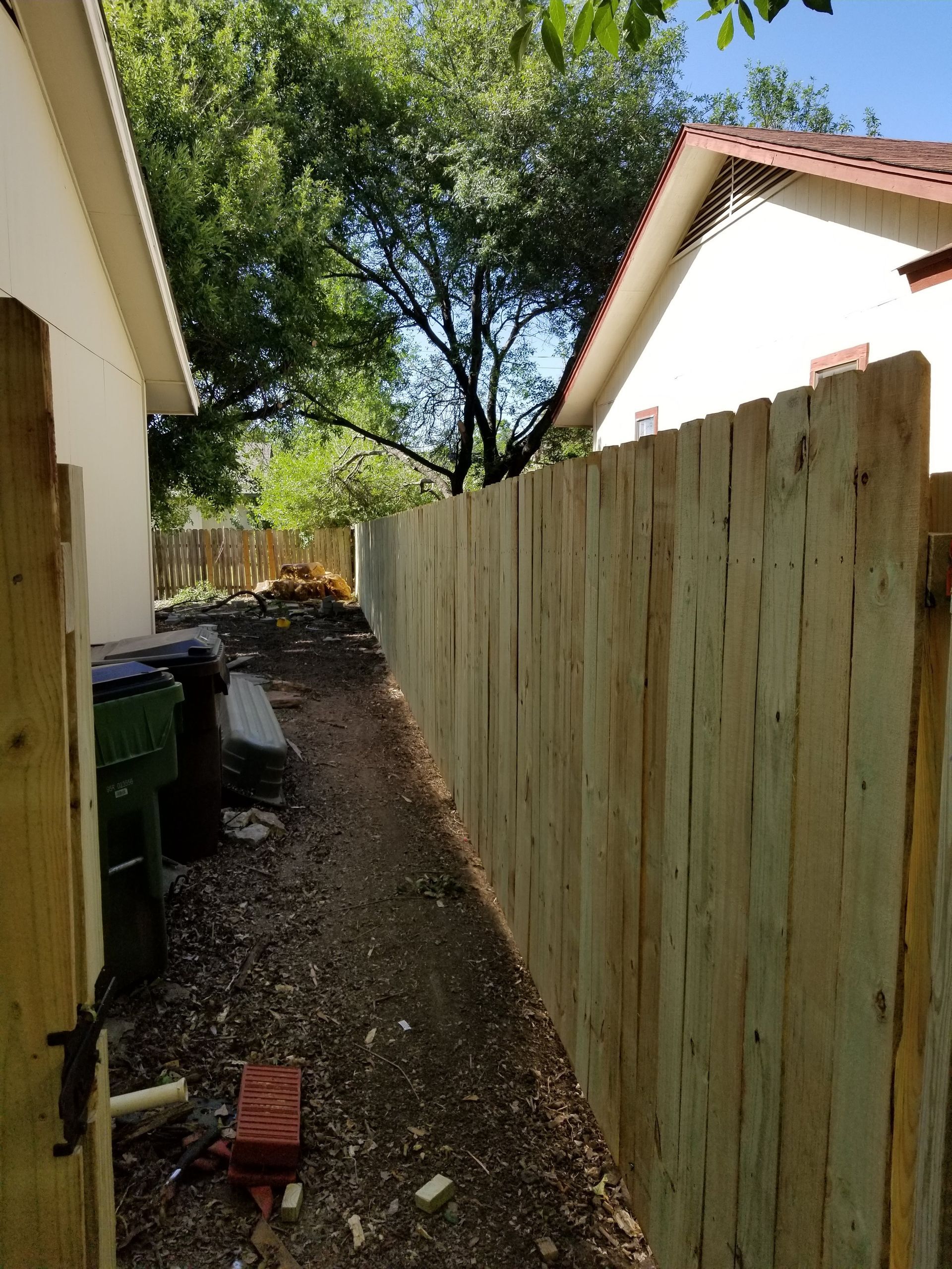 A wooden fence surrounds a dirt path leading to a house.