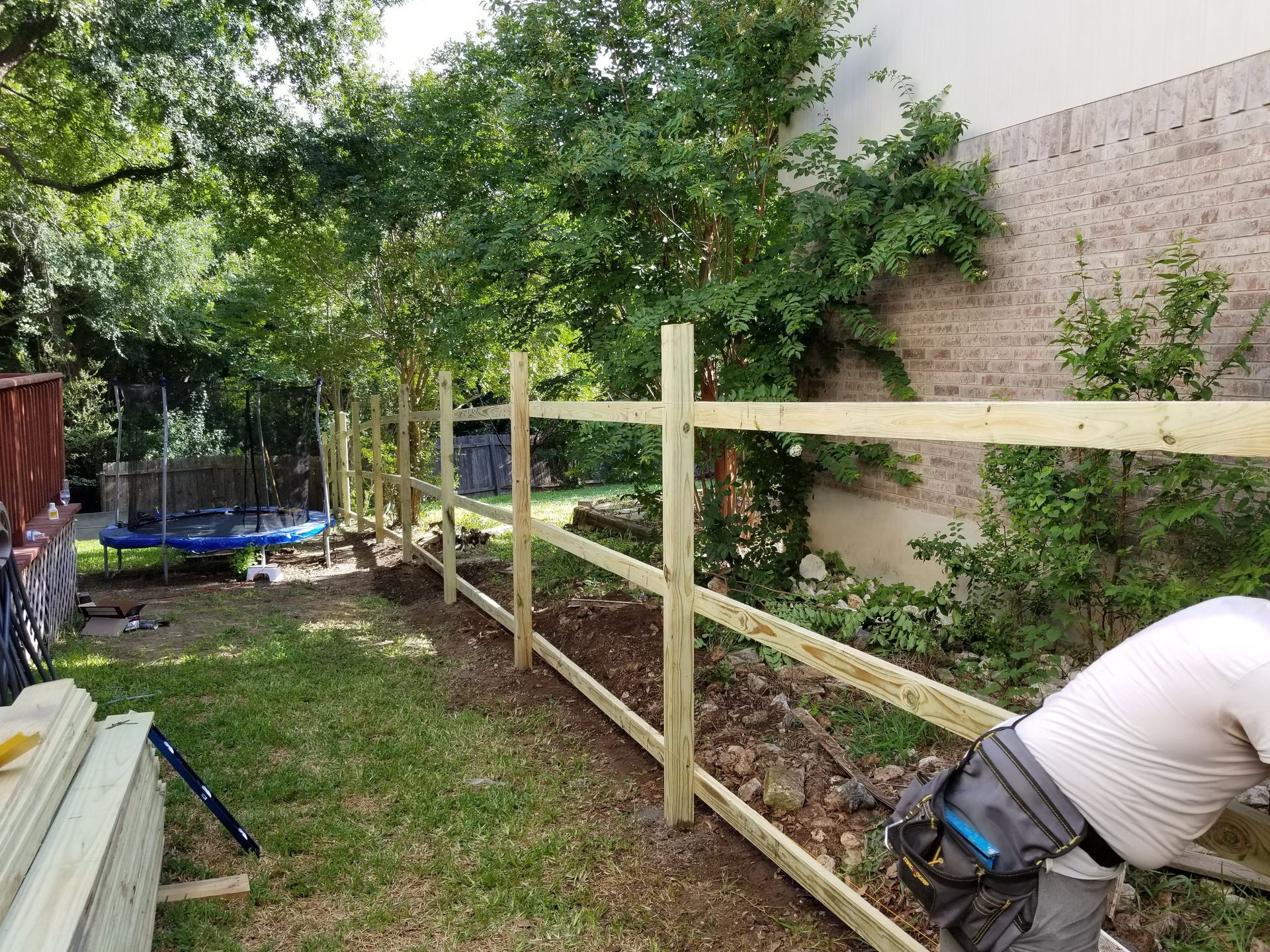 A man is working on a wooden fence in a backyard.