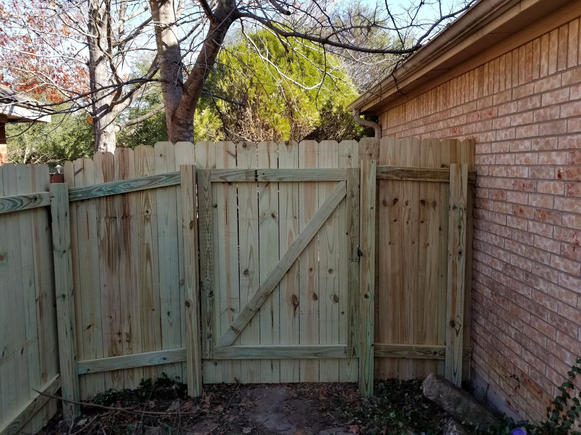 A wooden fence with a gate in front of a brick building.