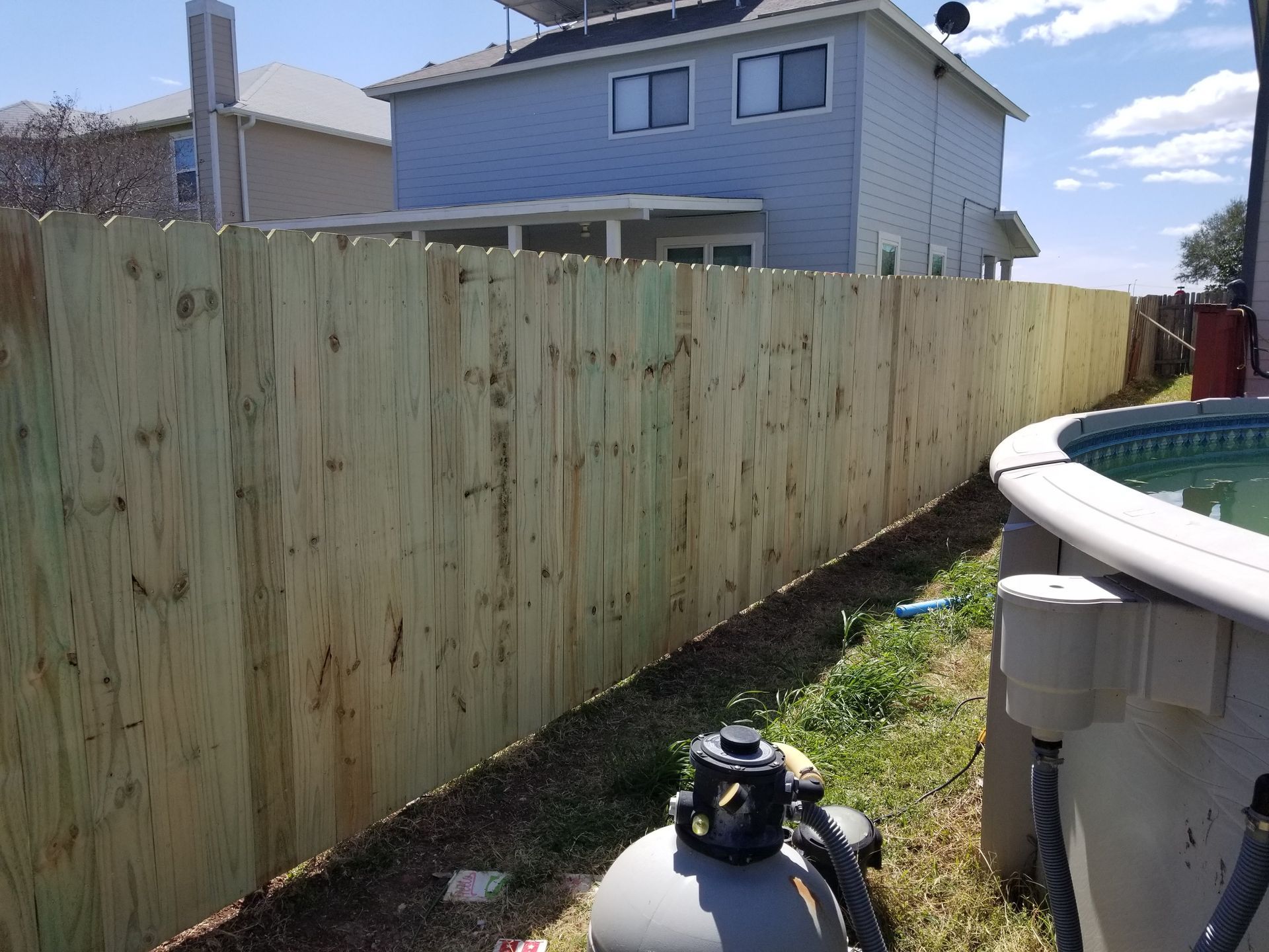 A wooden fence surrounds a pool and a house.