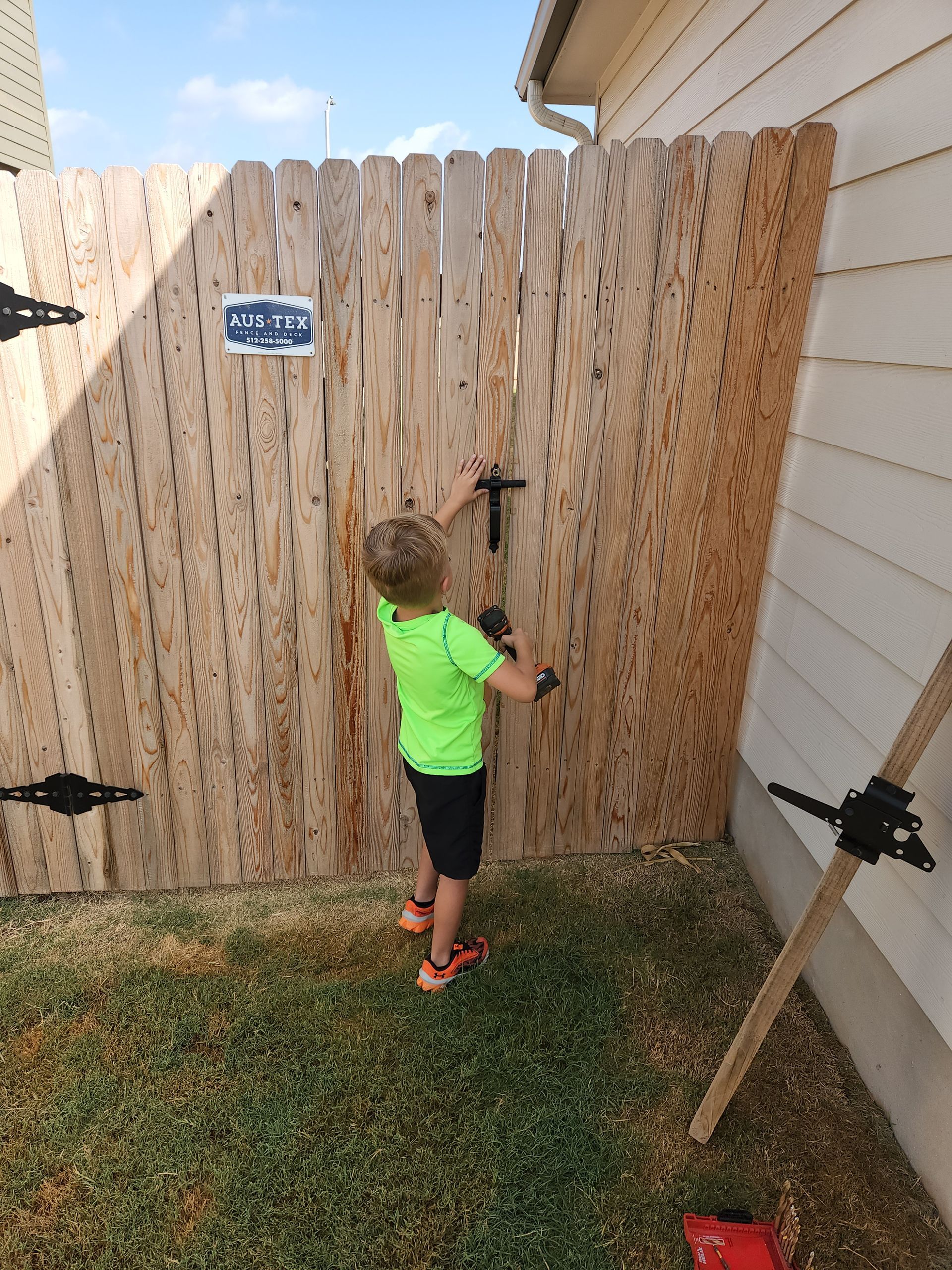 A young boy is standing next to a wooden fence holding a hammer.
