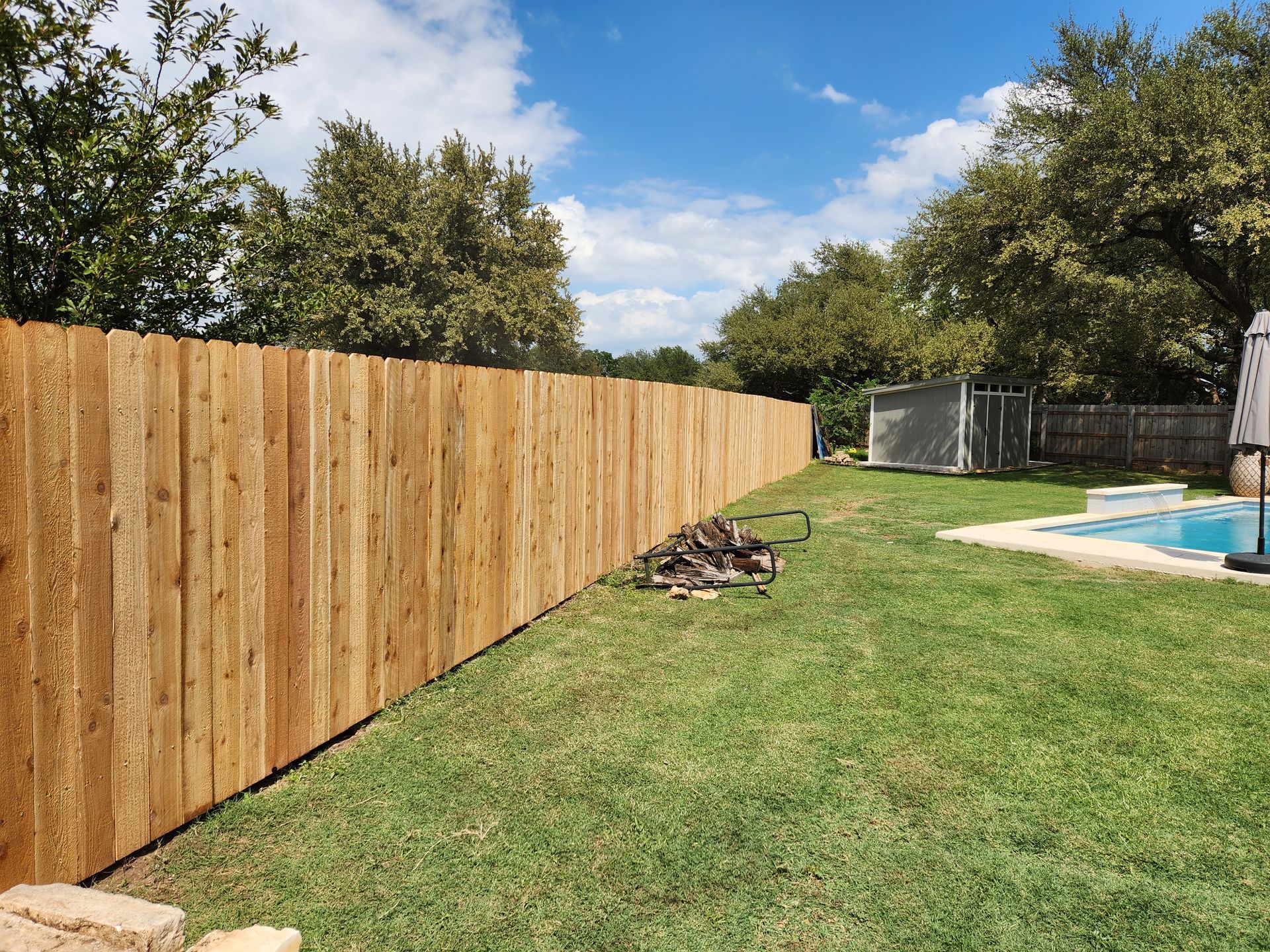 A wooden fence surrounds a lush green backyard next to a pool.
