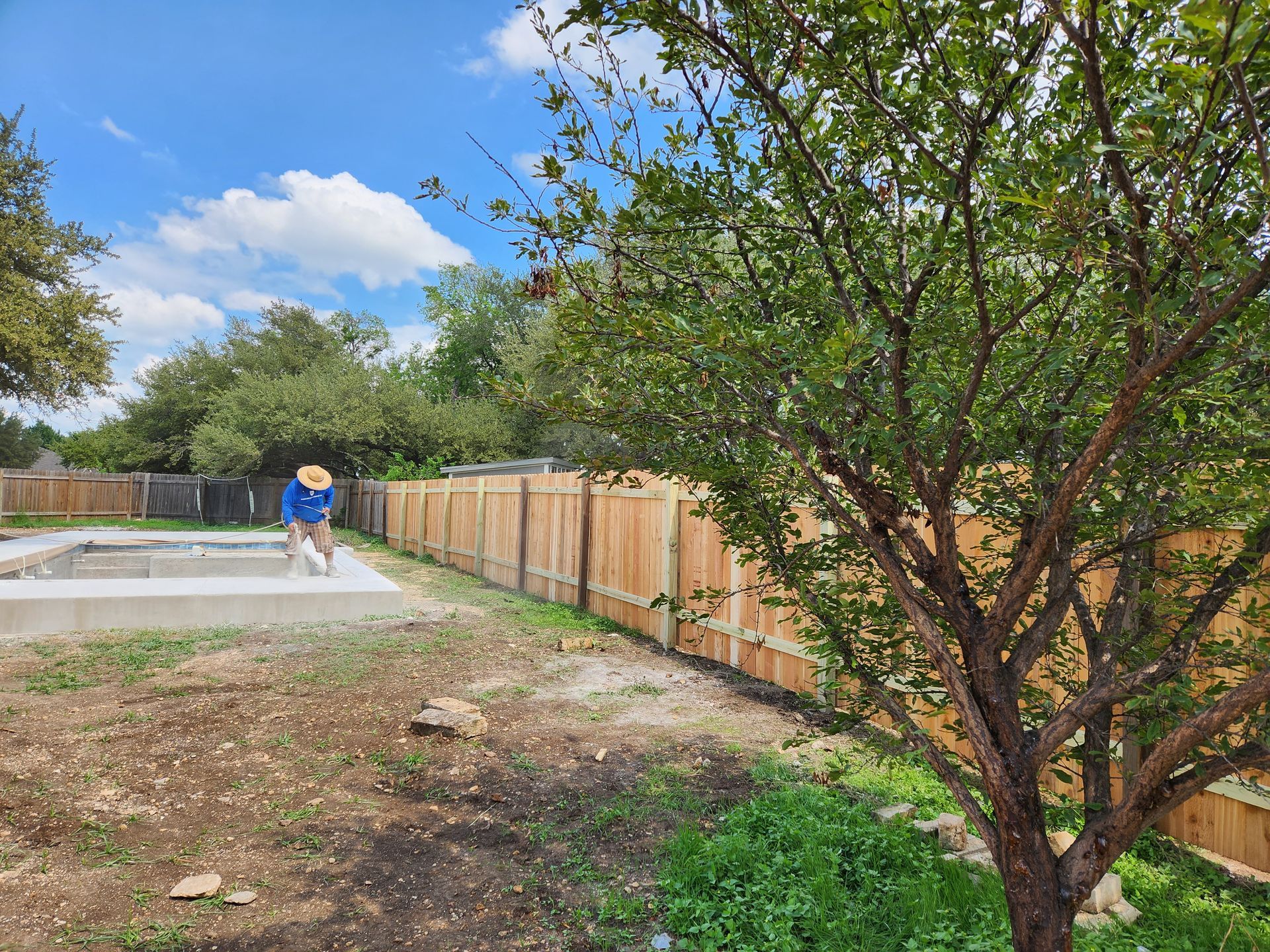 A man is standing next to a wooden fence in a backyard.