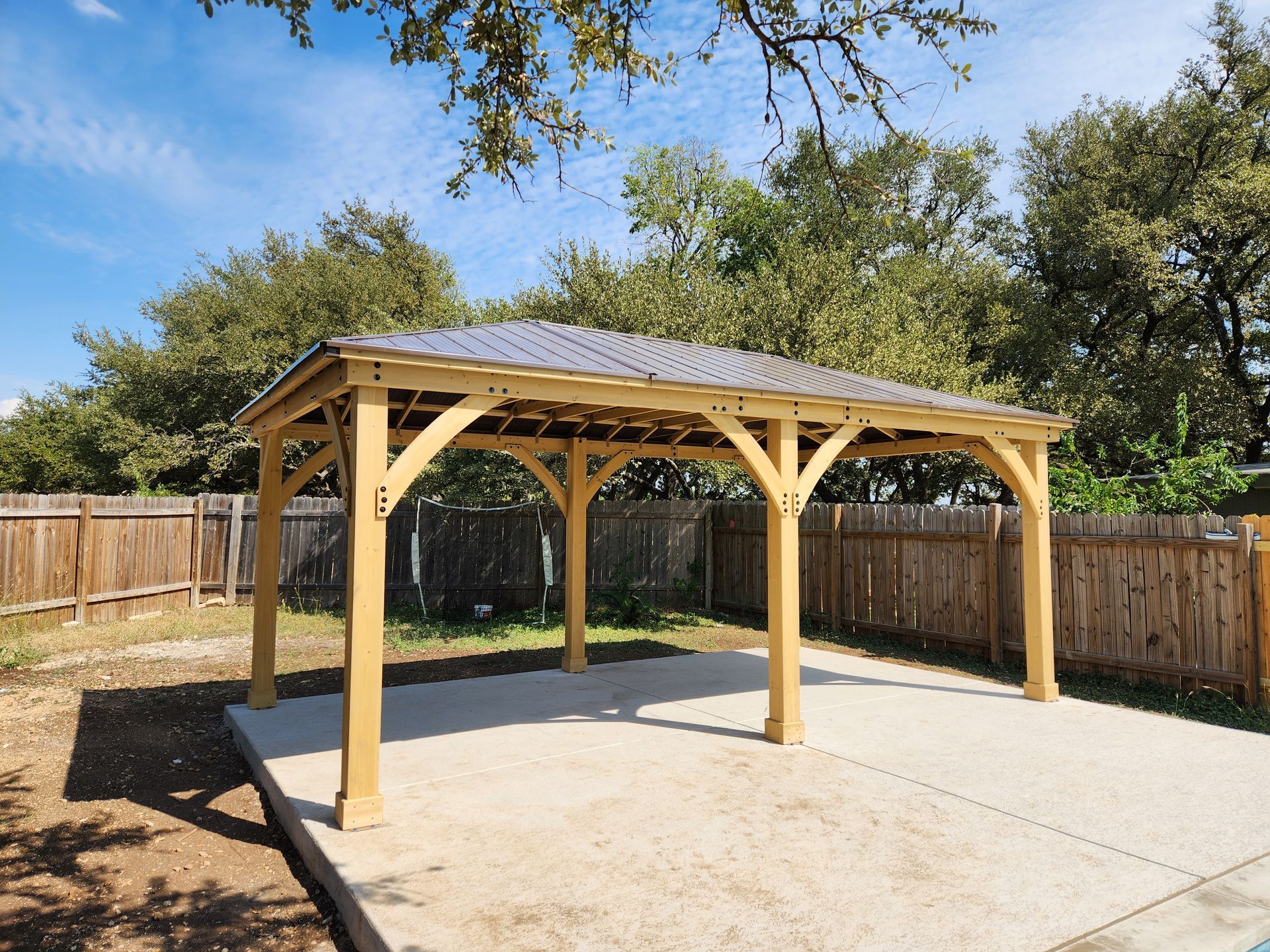 A wooden gazebo is sitting on top of a concrete base in a backyard.