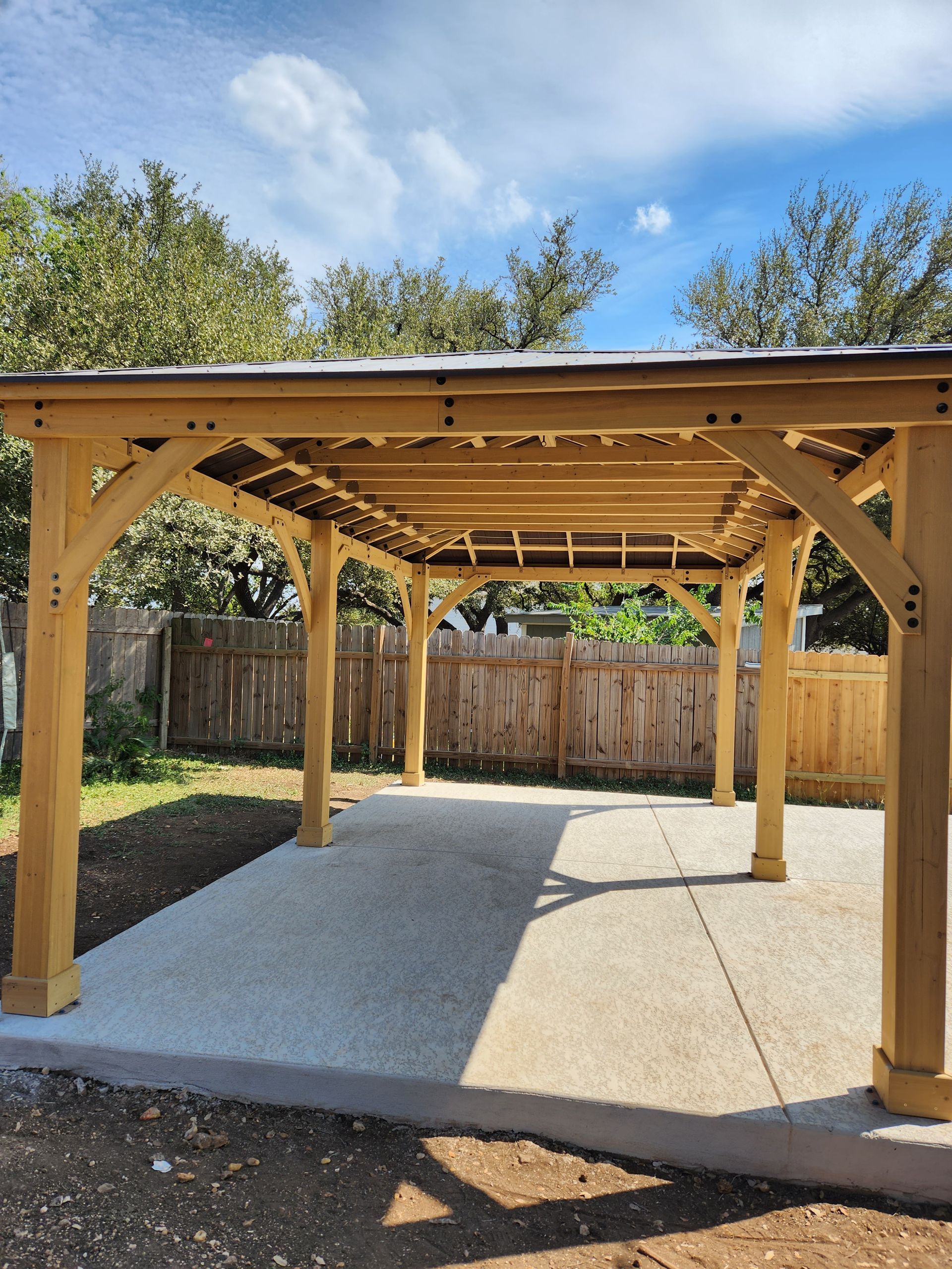 A wooden pergola is sitting on top of a concrete patio in a backyard.