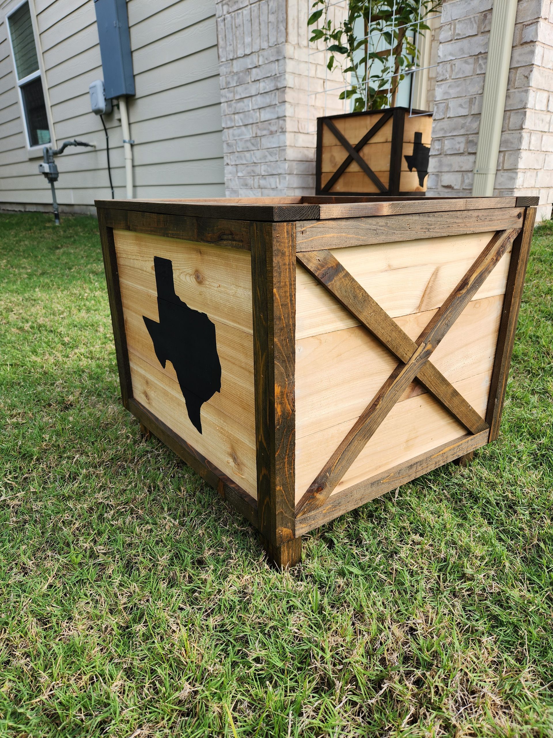 A wooden box with a texas map on it is sitting in the grass.