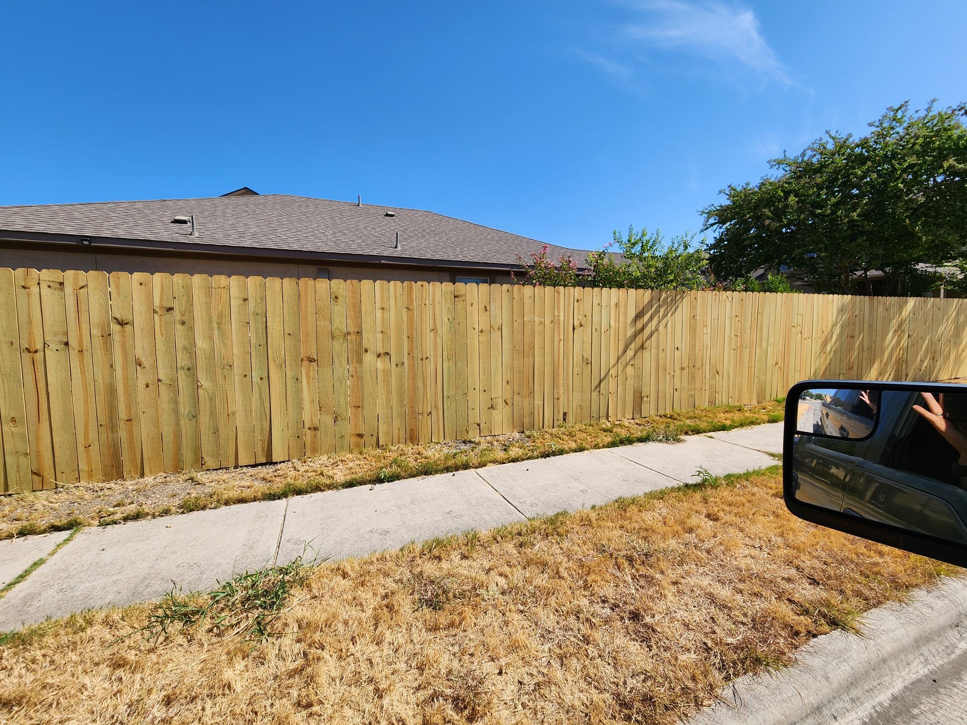 A wooden fence is sitting next to a sidewalk in front of a house.