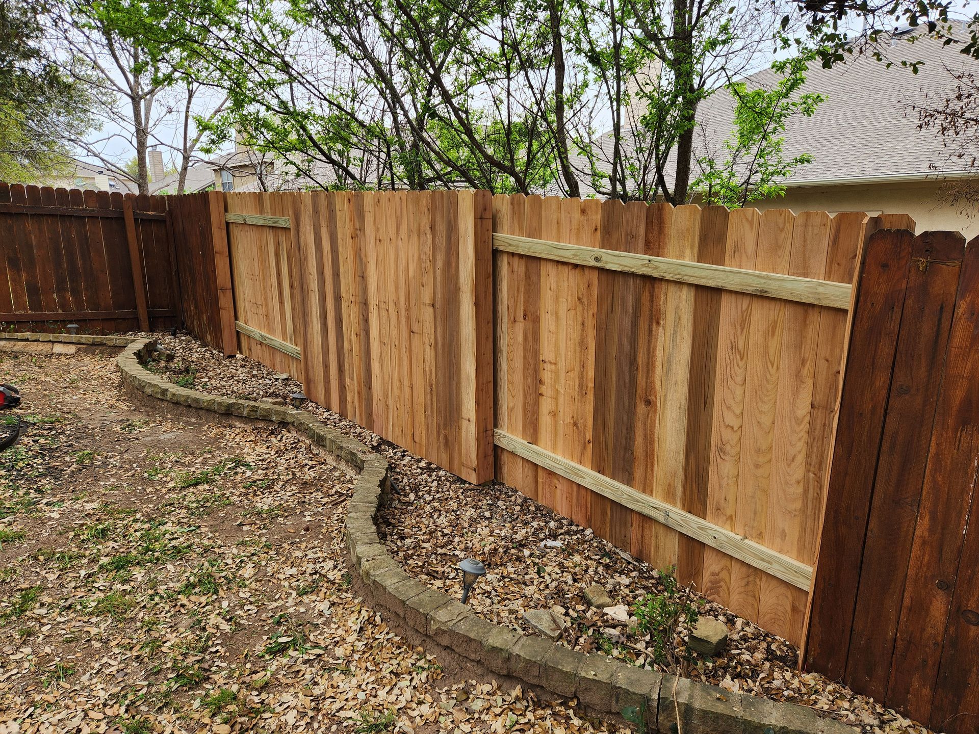 A wooden fence is in the backyard of a house.