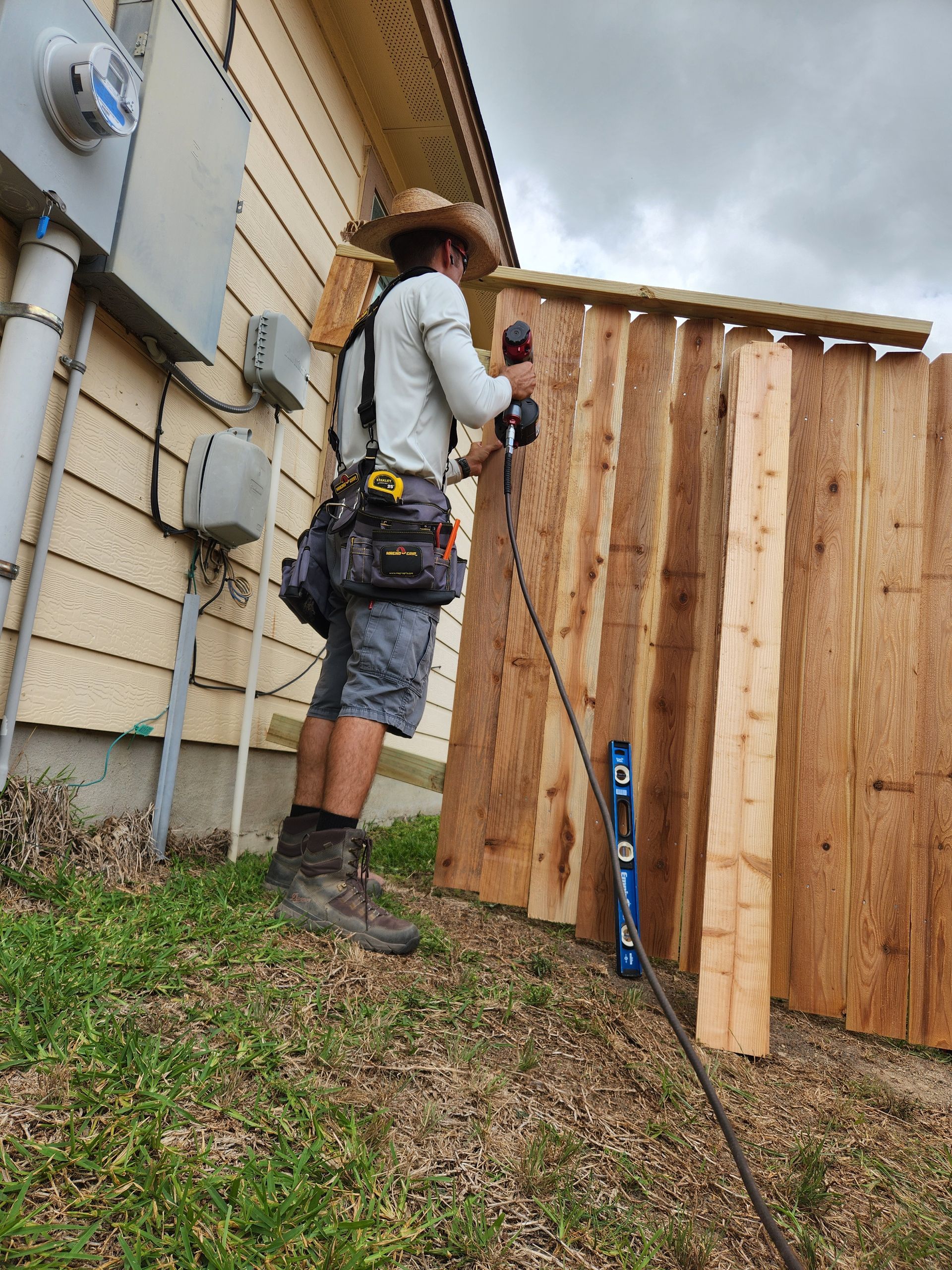 A man is working on a wooden fence in front of a house.