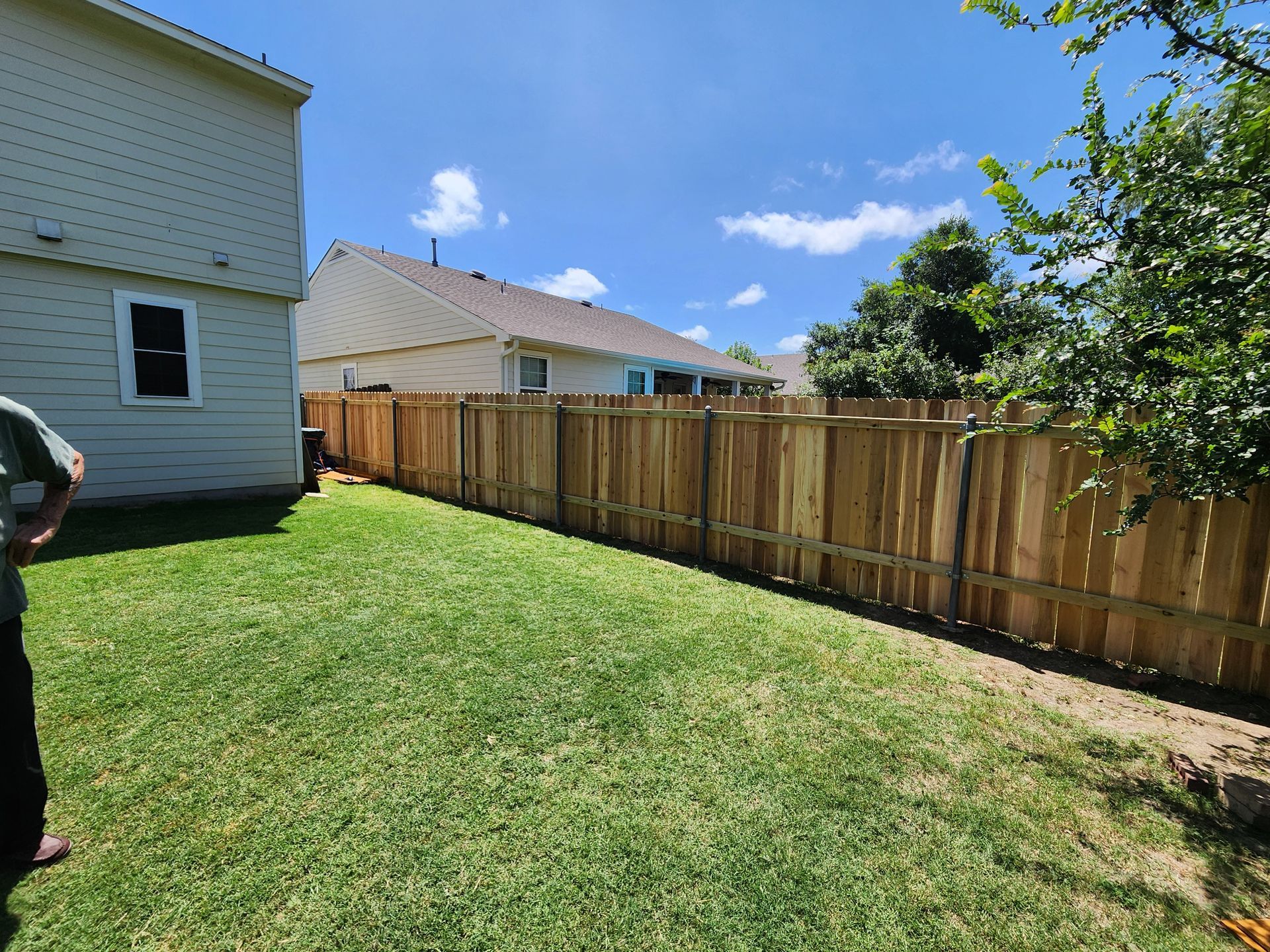 A man is standing in a backyard next to a wooden fence.