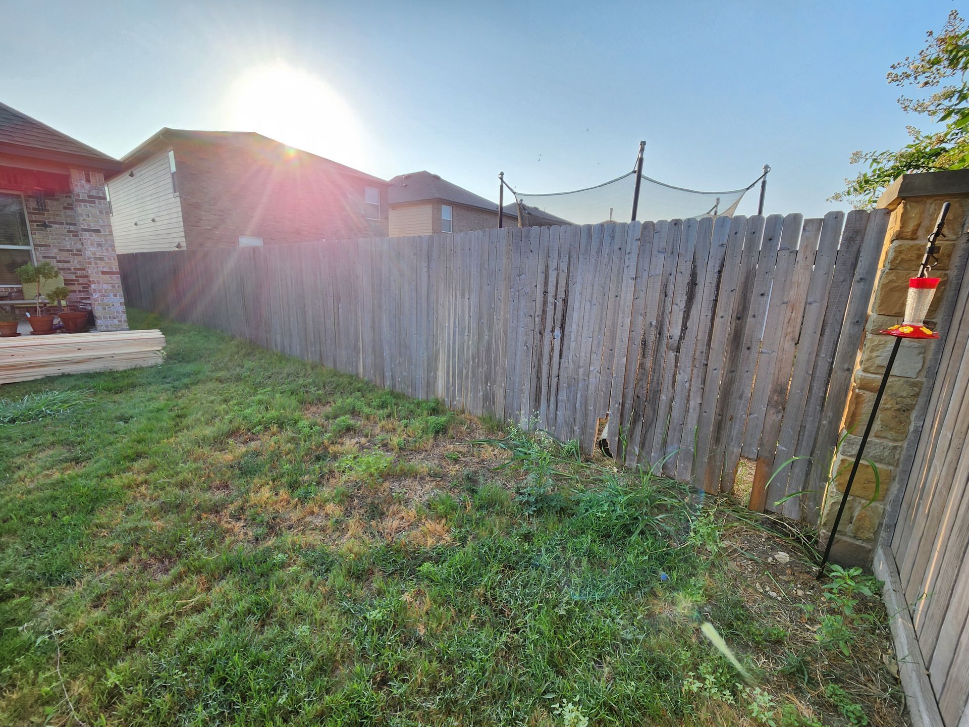 A wooden fence surrounds a lush green yard with a house in the background.