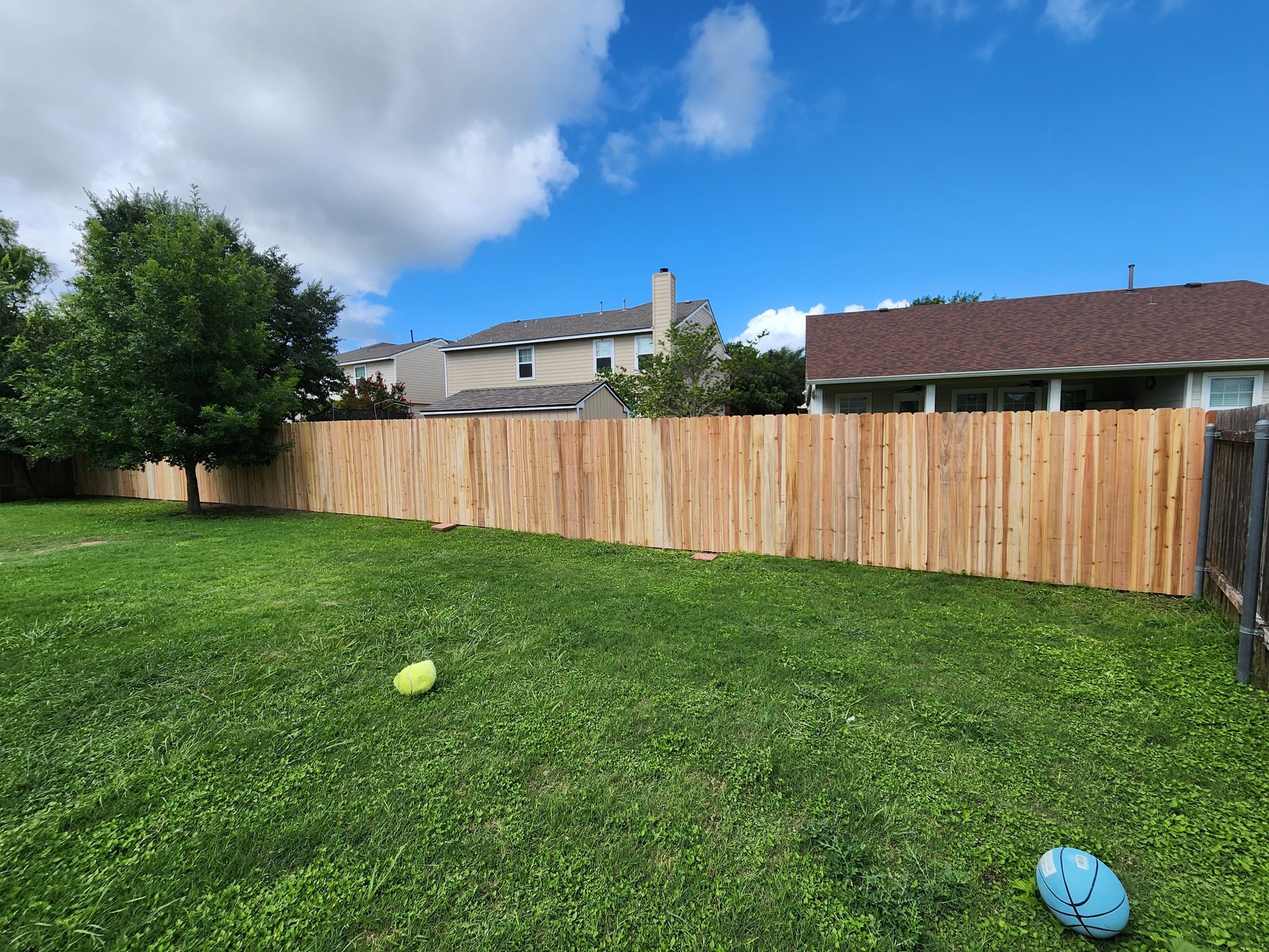 There is a wooden fence in the backyard with a frisbee in the grass.