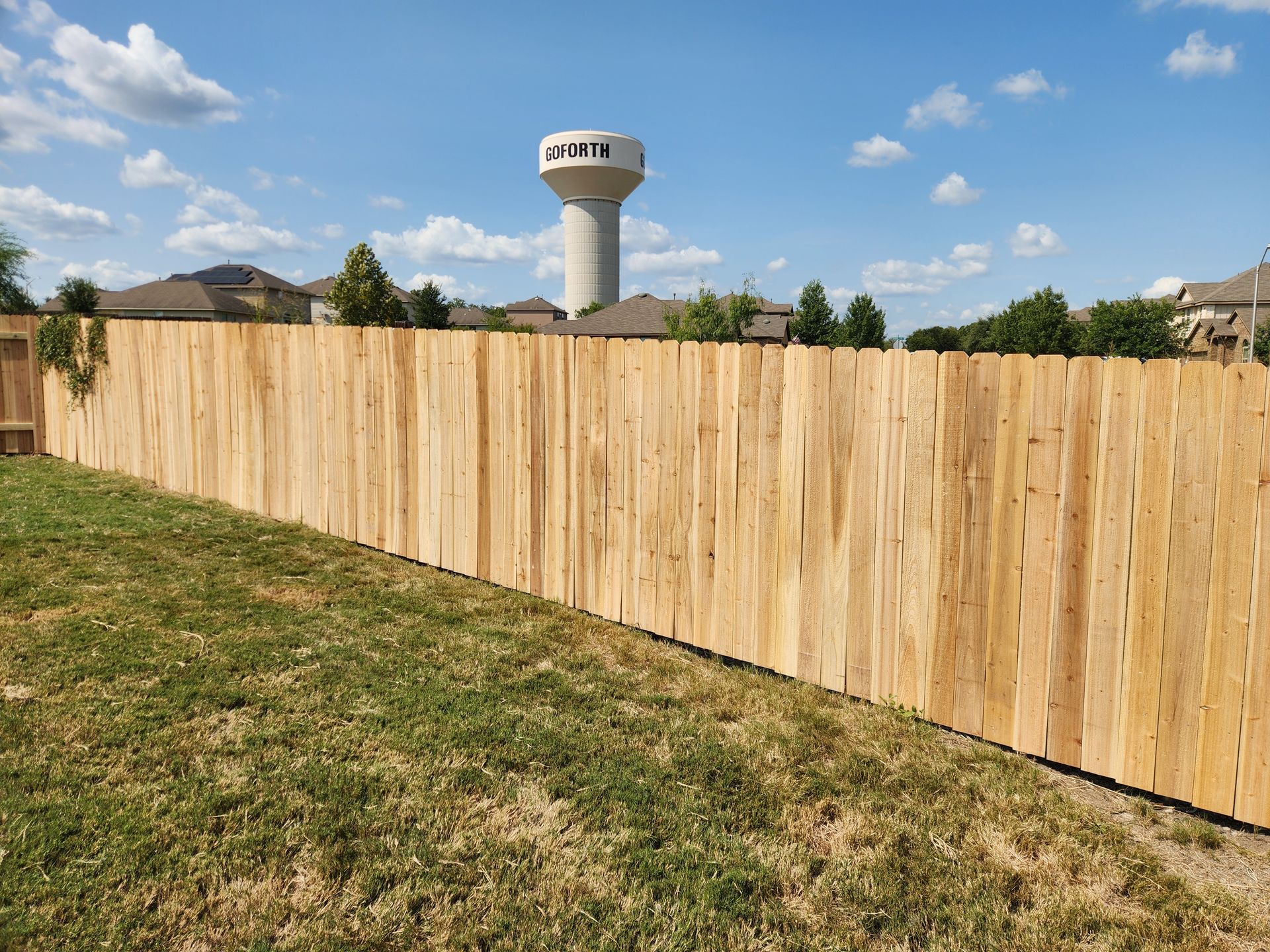 A wooden fence in a backyard with a water tower in the background.