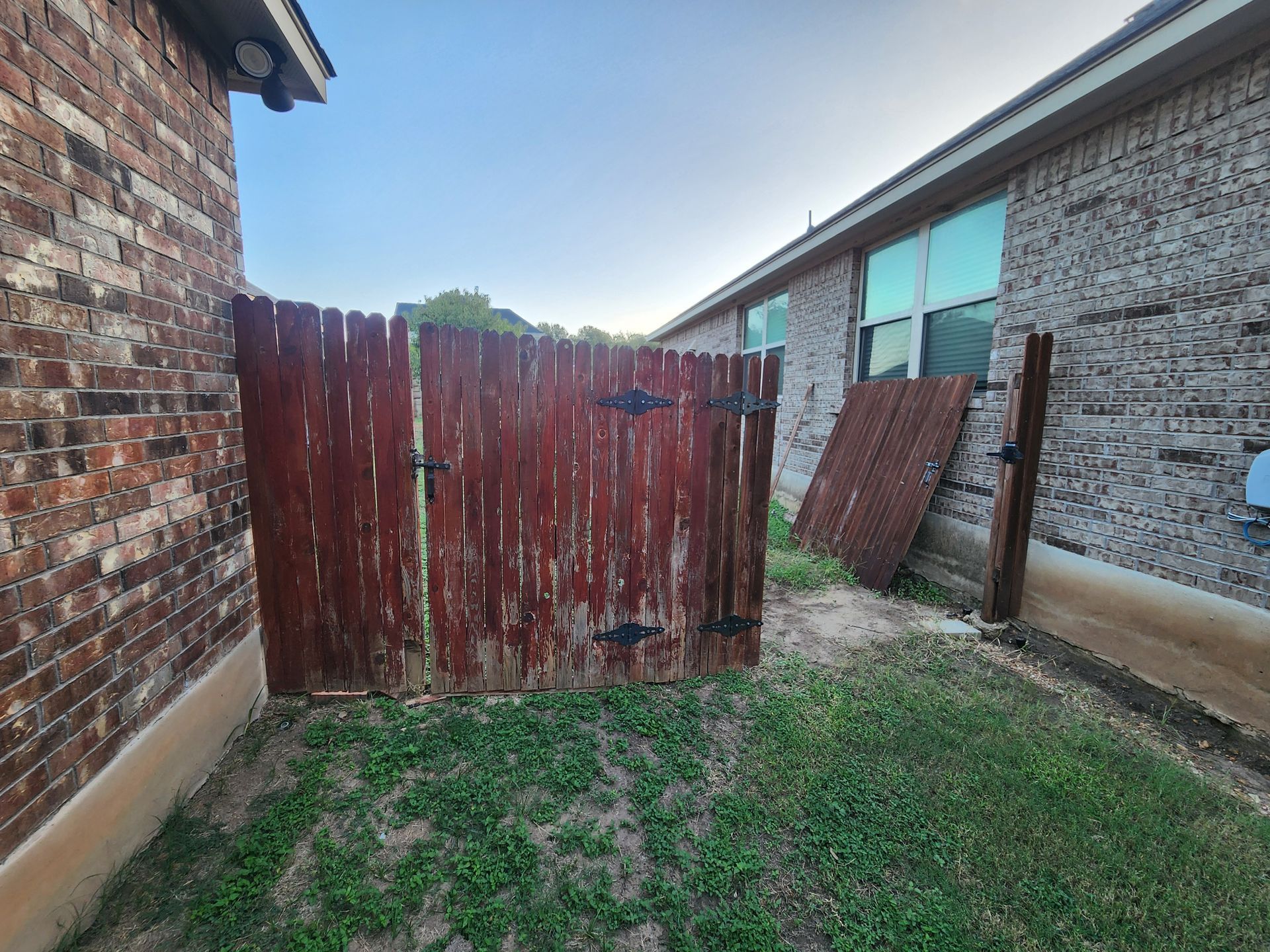 A wooden fence is in the backyard of a brick house.