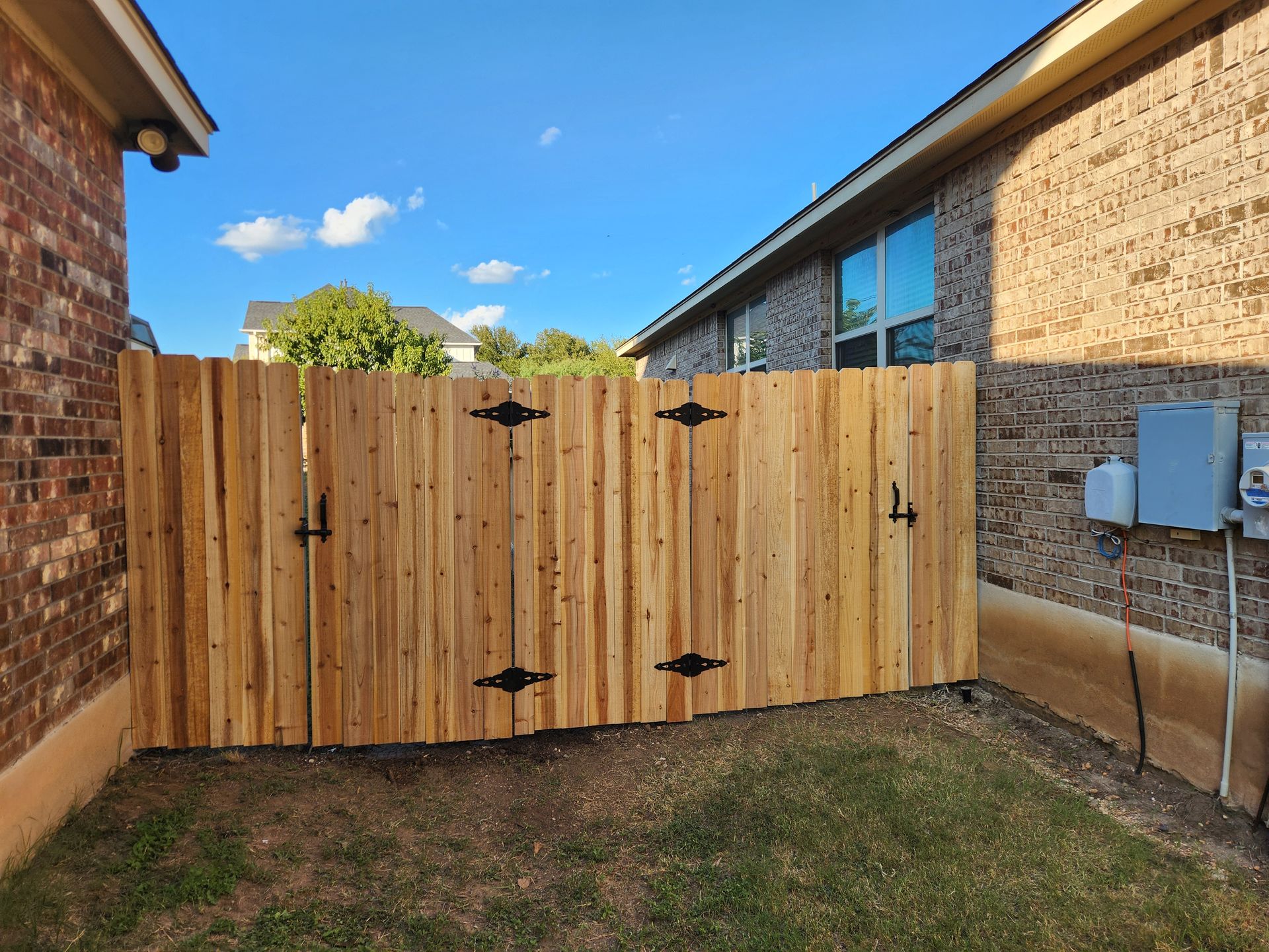 A wooden fence is in the backyard of a brick house.