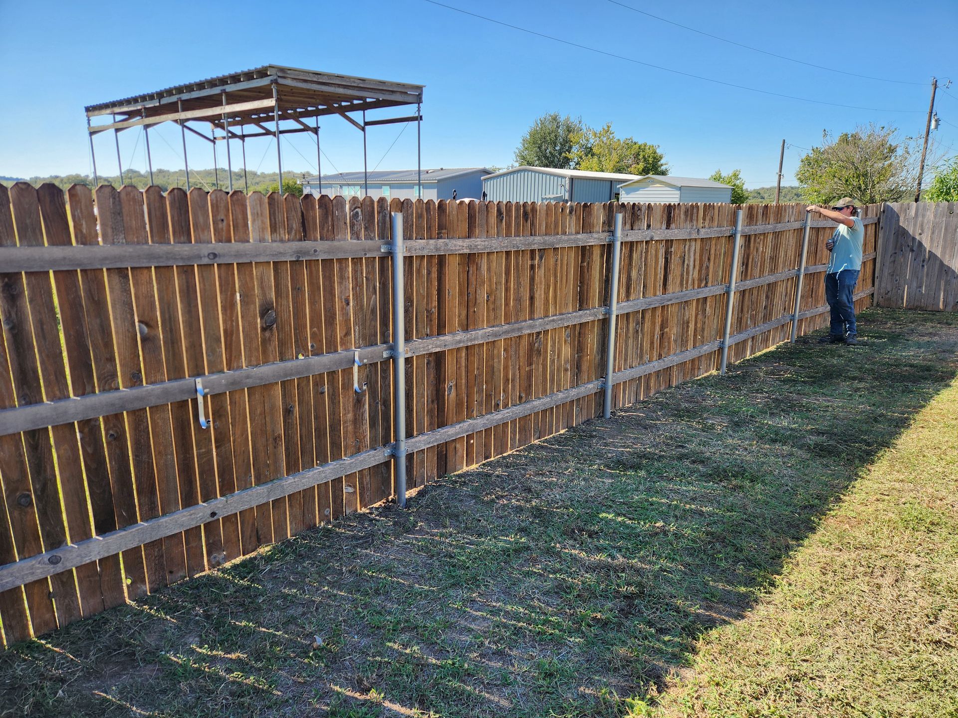 A man is standing in front of a wooden fence.
