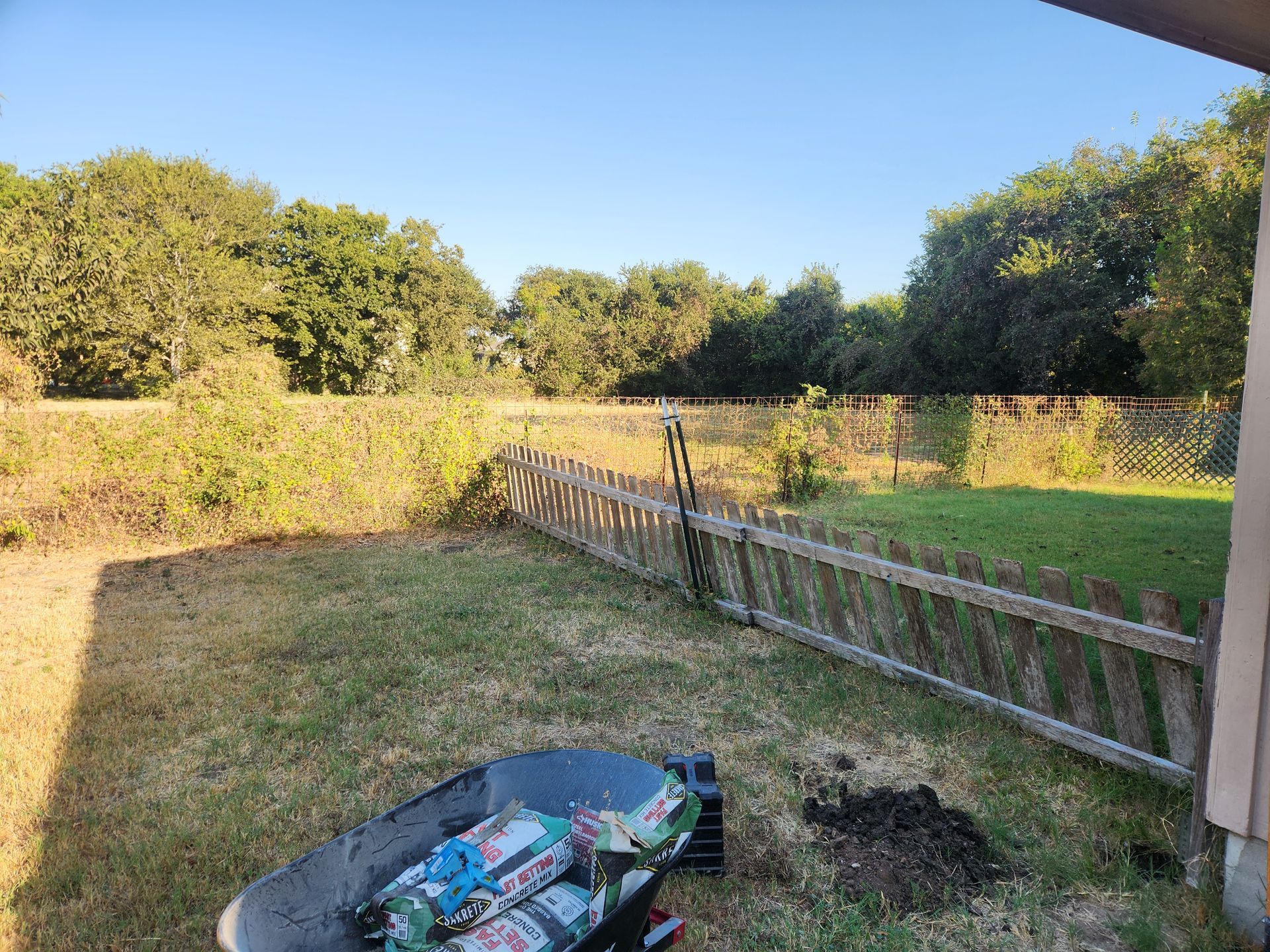 A wheelbarrow is sitting in the grass next to a wooden fence.