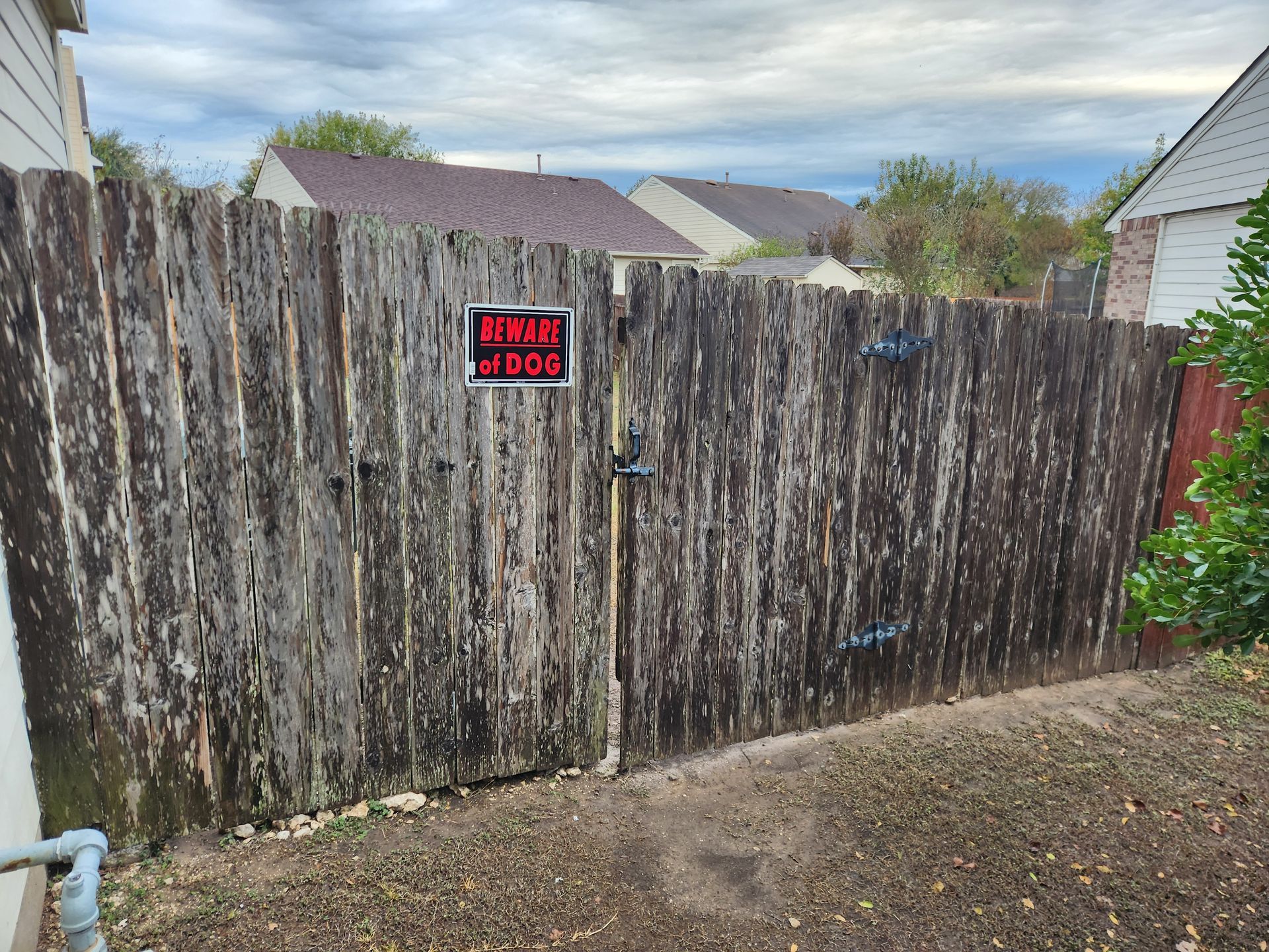 A wooden fence with a sign on it and a house in the background.