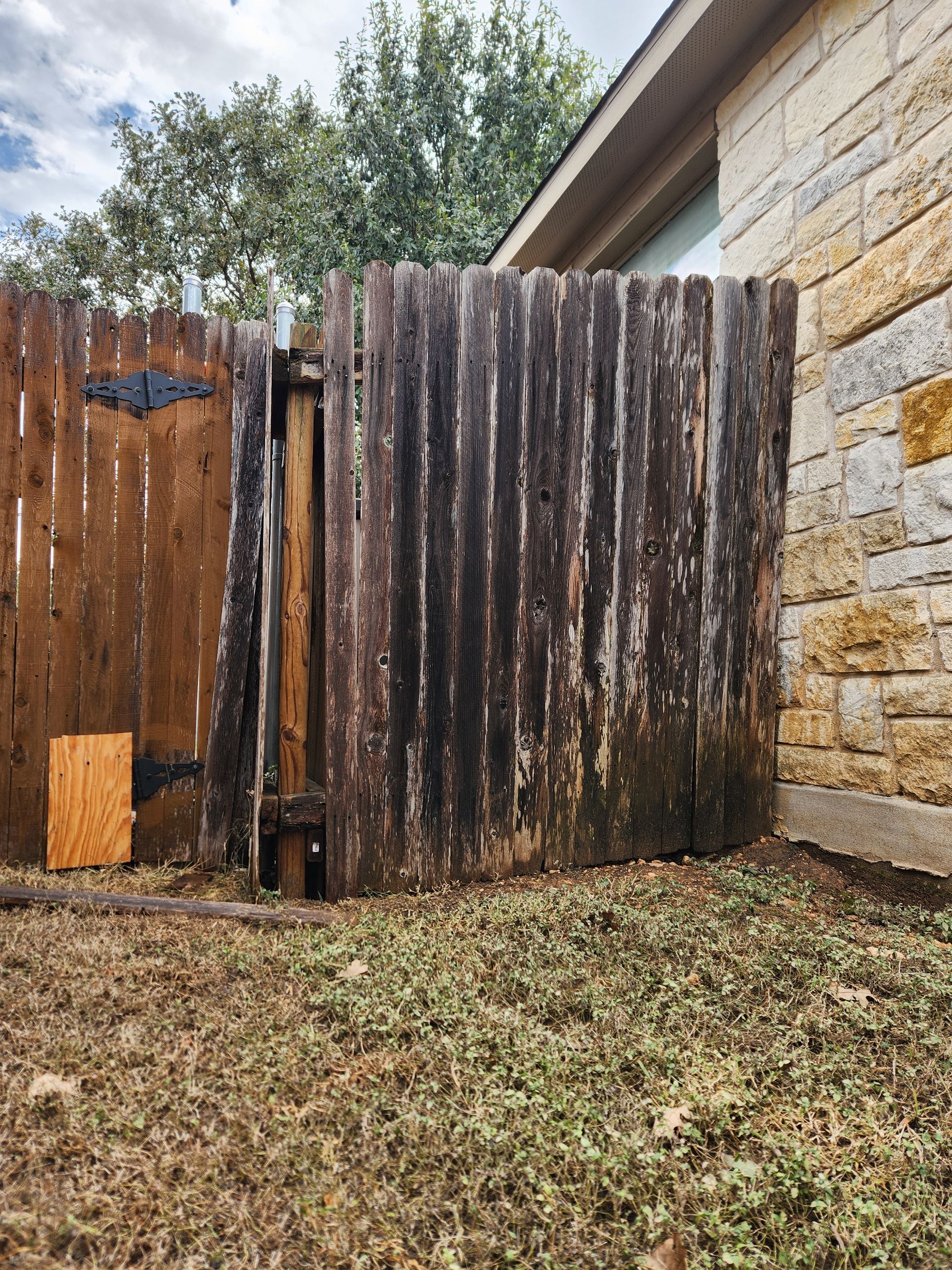 A wooden fence is sitting in the grass next to a stone wall.