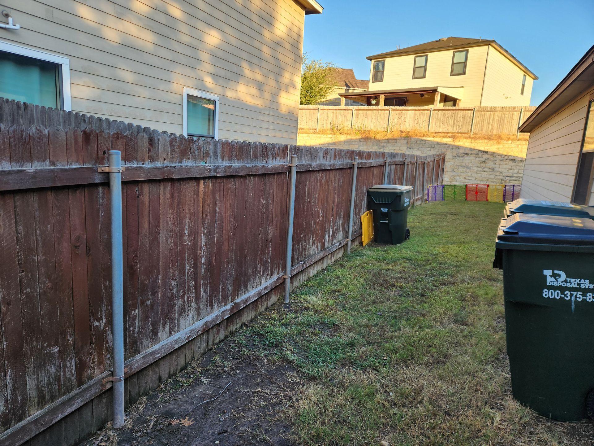 A wooden fence with a trash can in front of it.