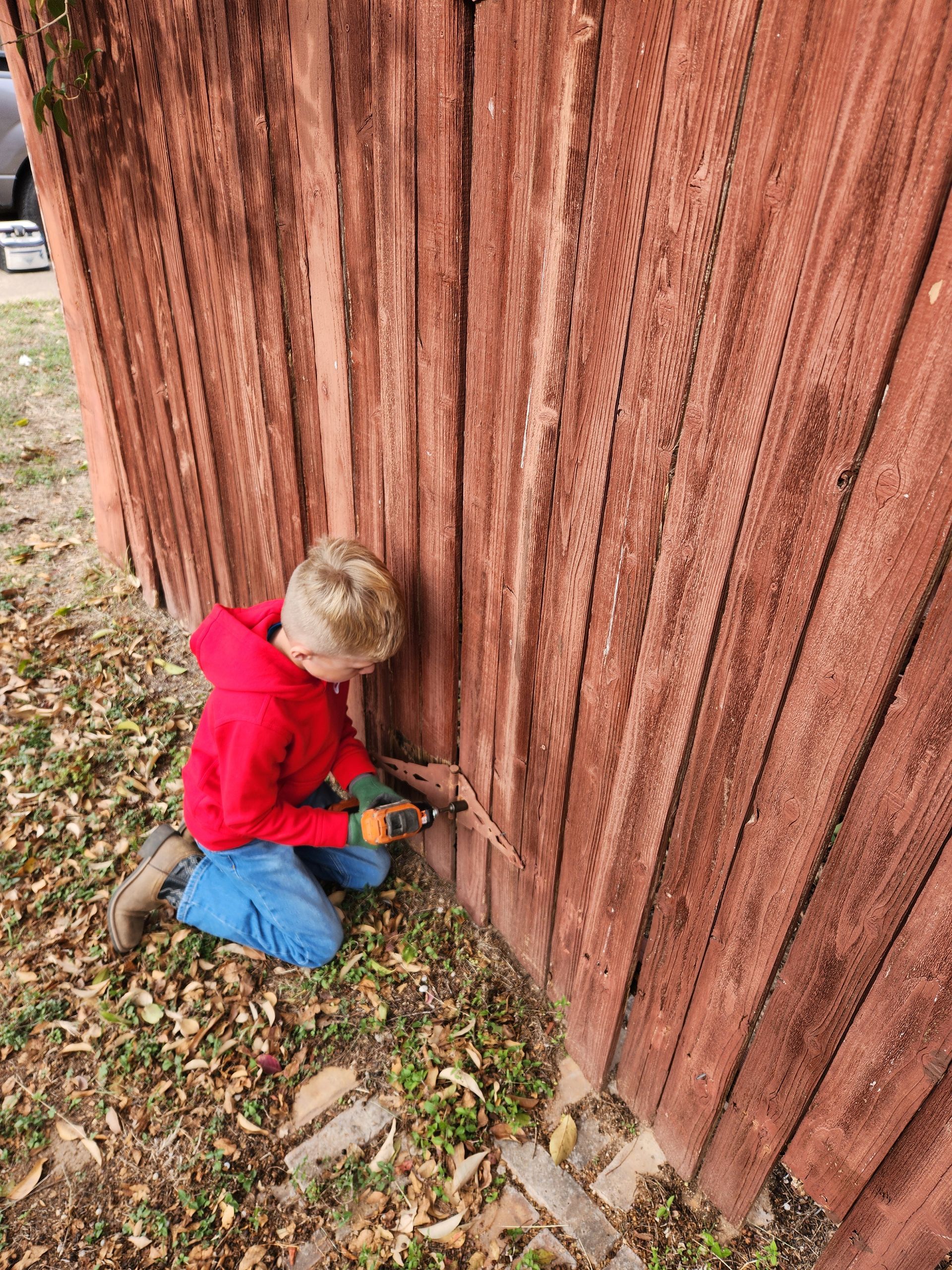A young boy is kneeling down next to a wooden fence.