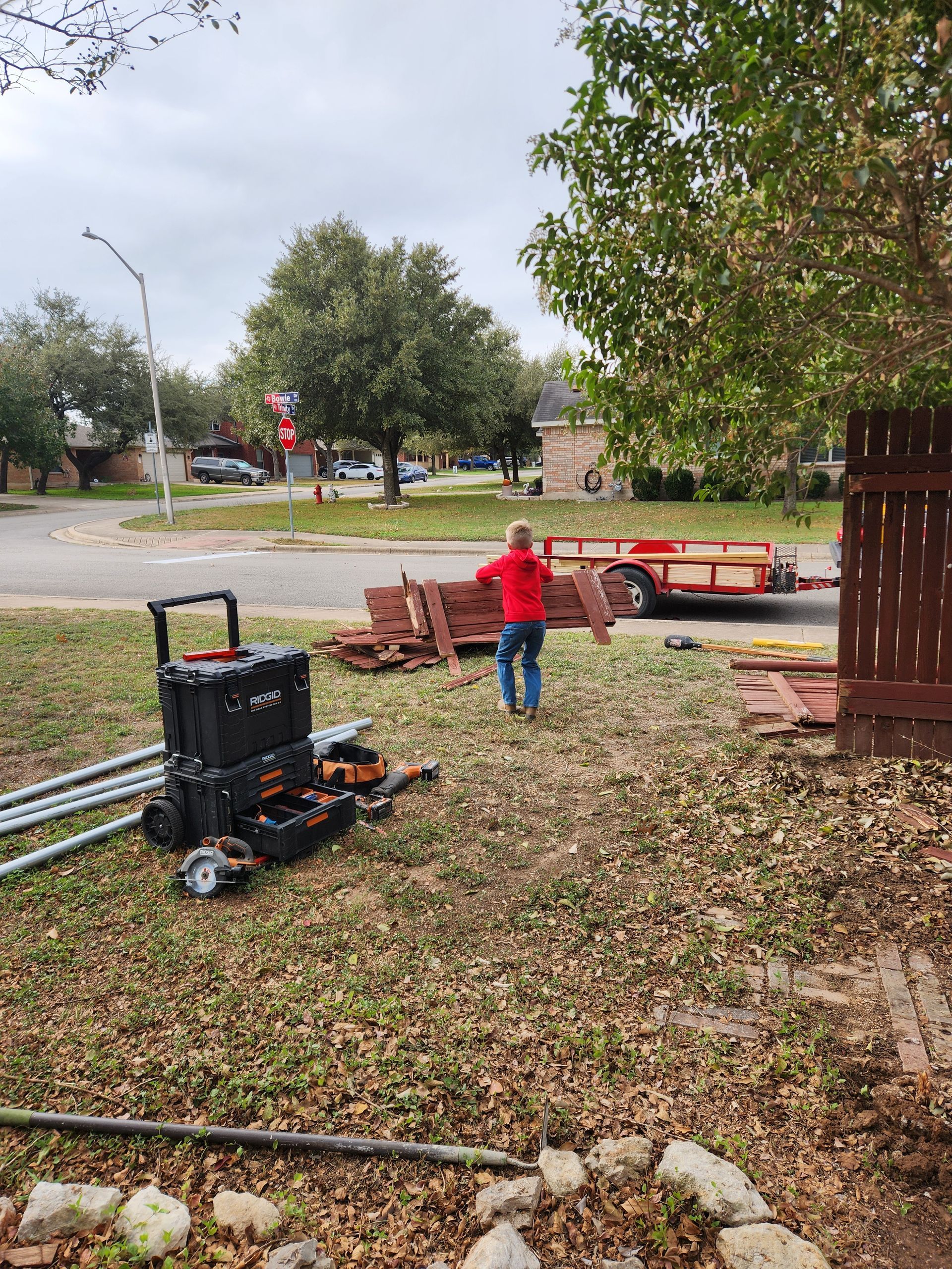 A man is standing in a yard holding a piece of wood.