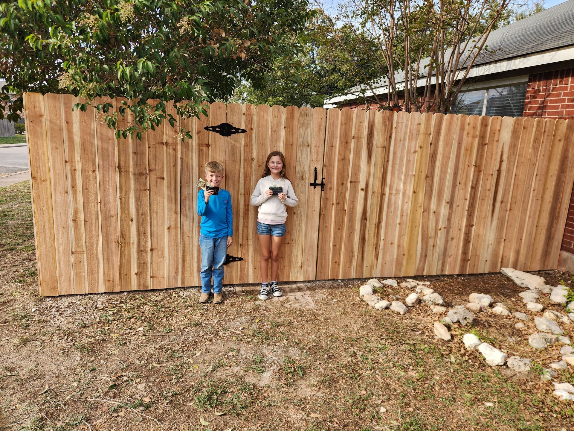 A boy and a girl are standing in front of a wooden fence.