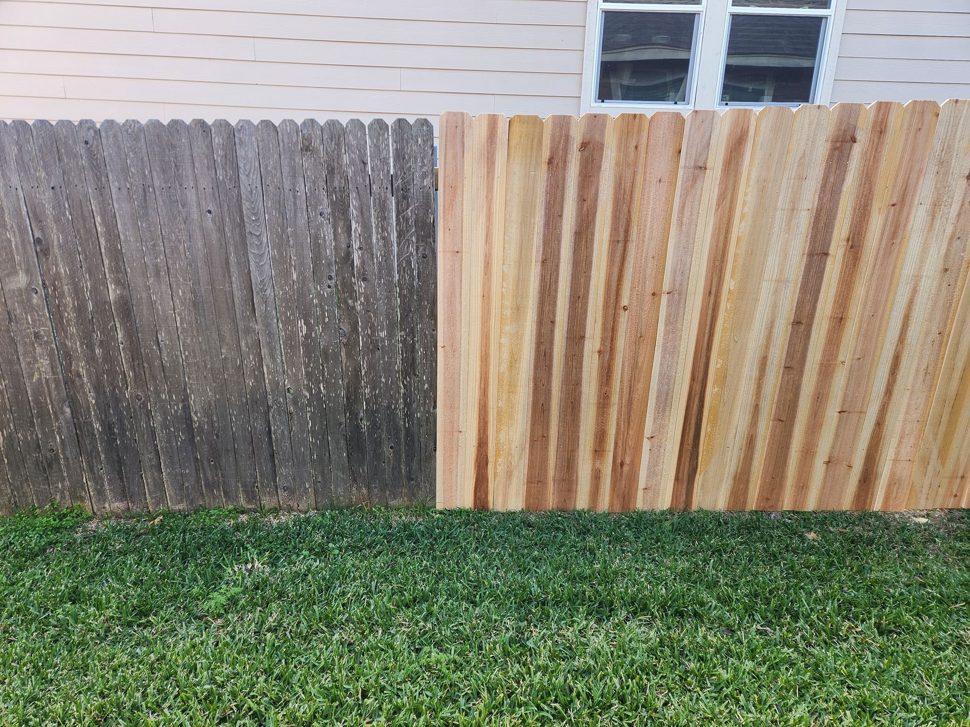 A wooden fence is sitting on top of a lush green lawn next to a house.