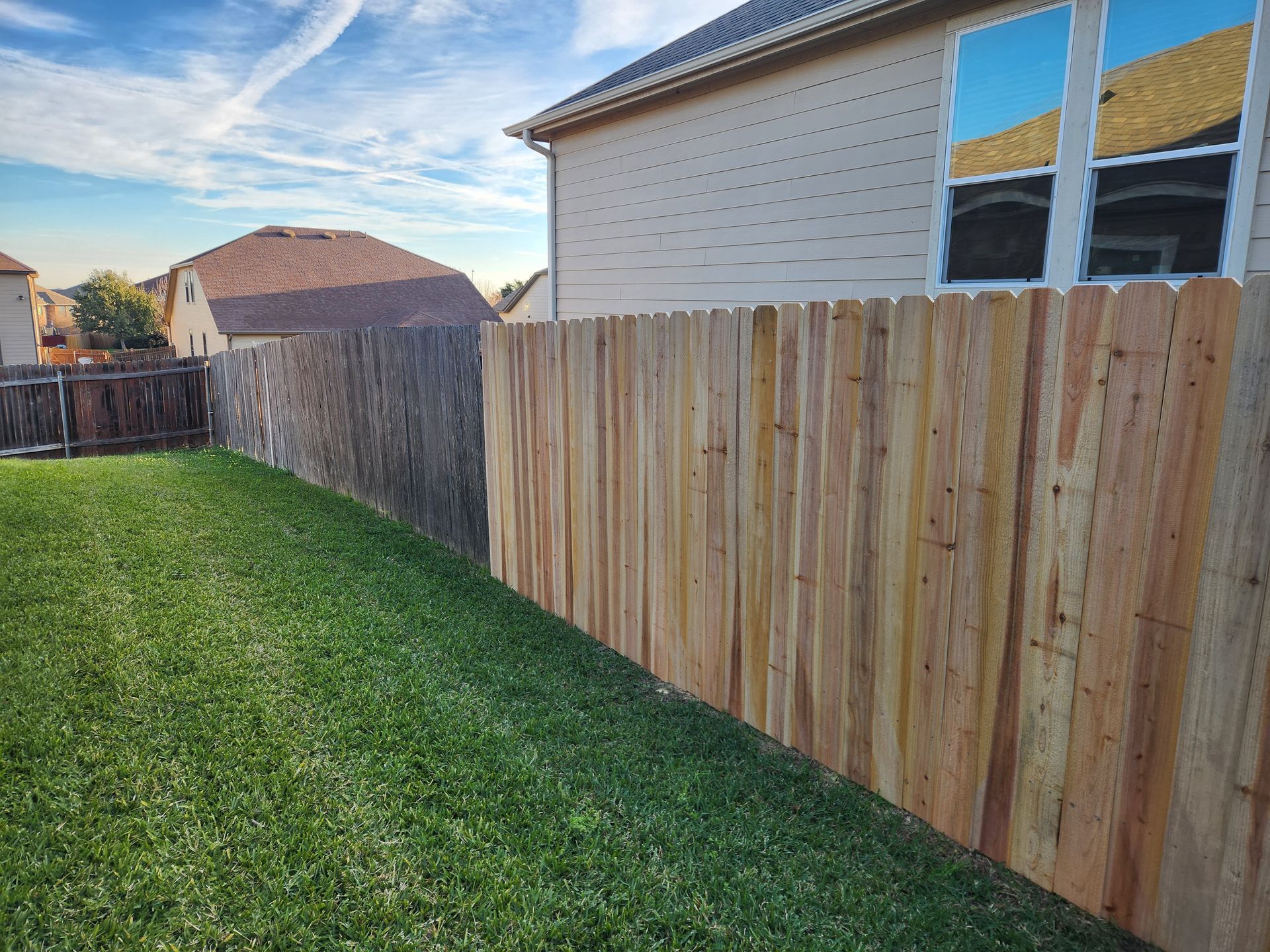 A wooden fence is in the backyard of a house.