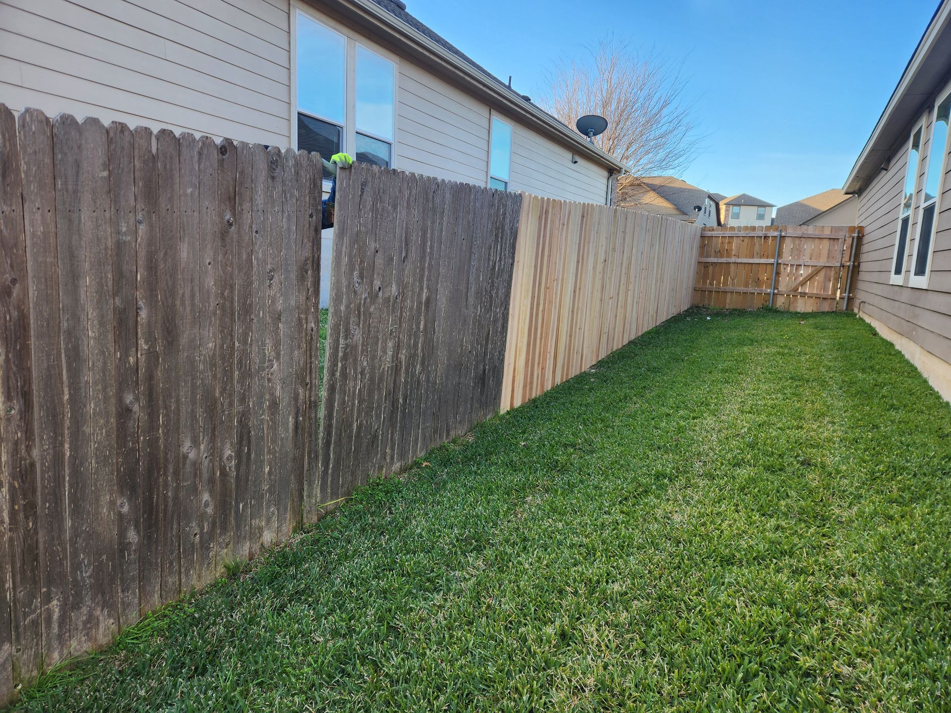 The backyard of a house with a wooden fence and a lush green lawn.