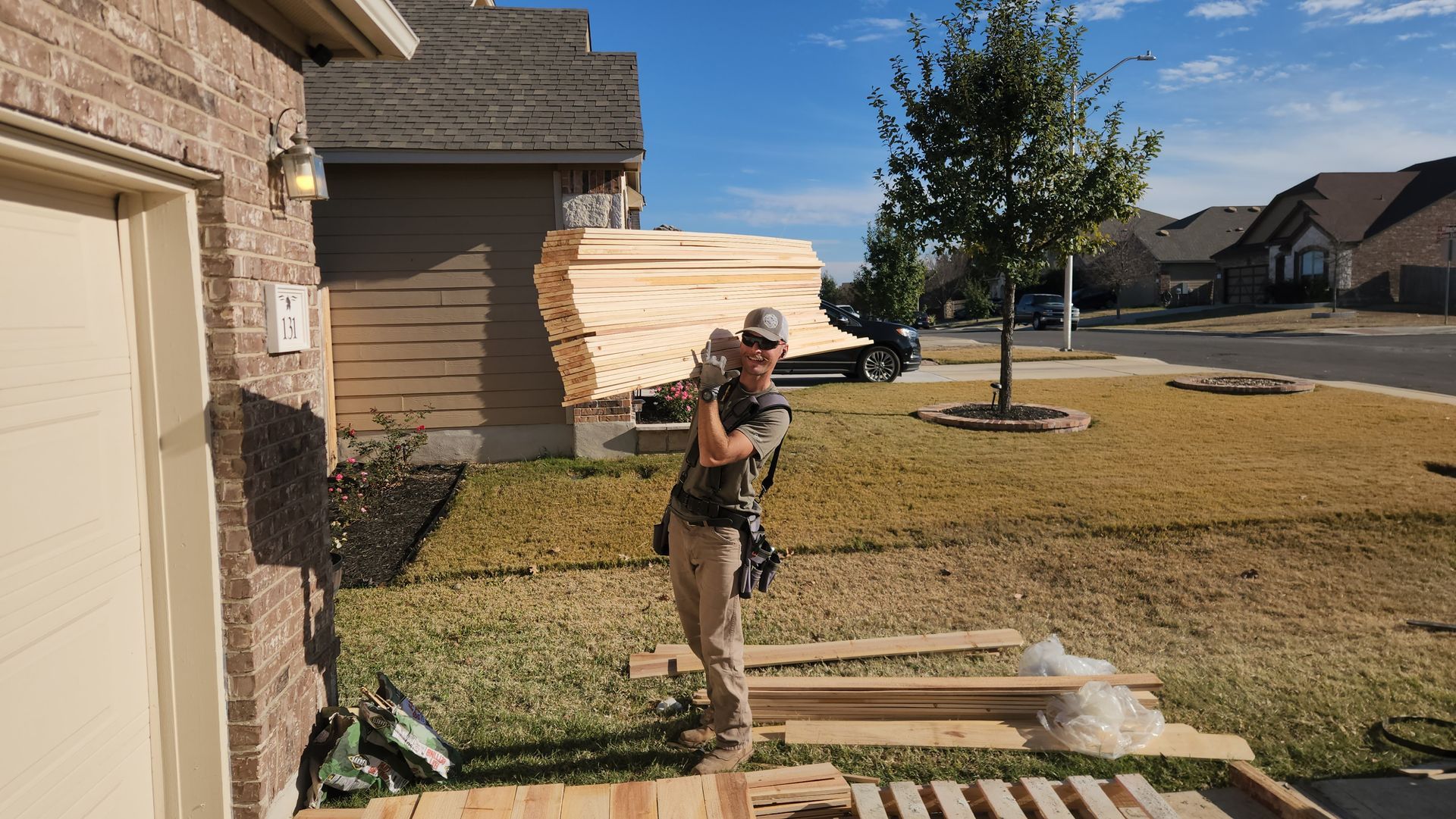 A man is standing next to a pile of wood in front of a house.