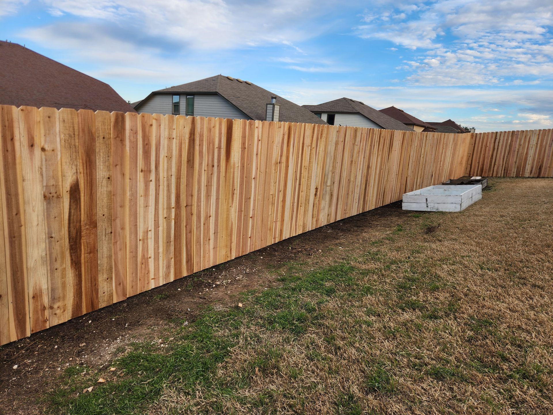 A wooden fence is in the backyard of a house.