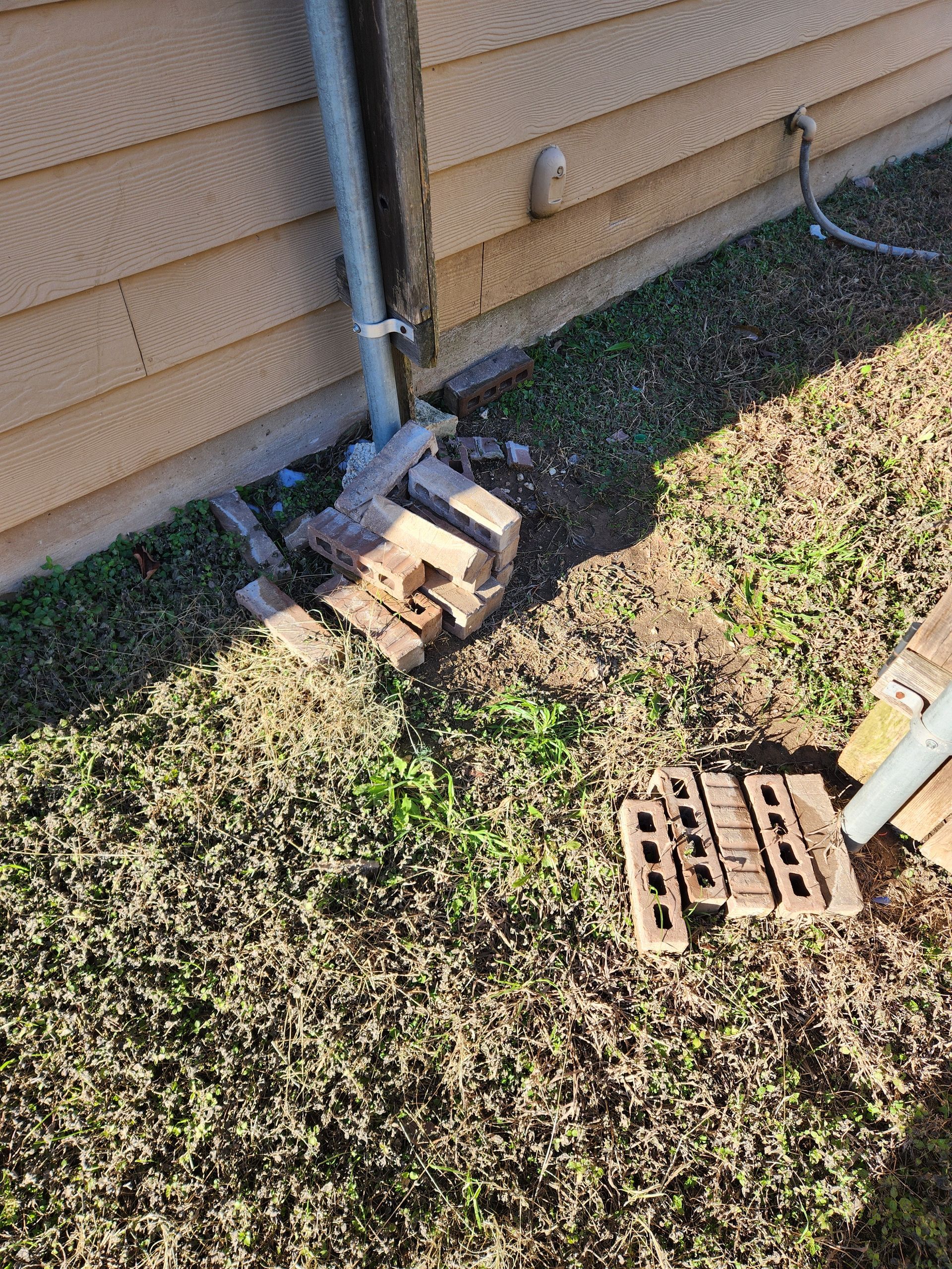 A pile of bricks is sitting in the grass next to a house.