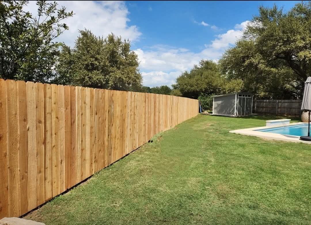 A wooden fence surrounds a lush green yard next to a swimming pool.