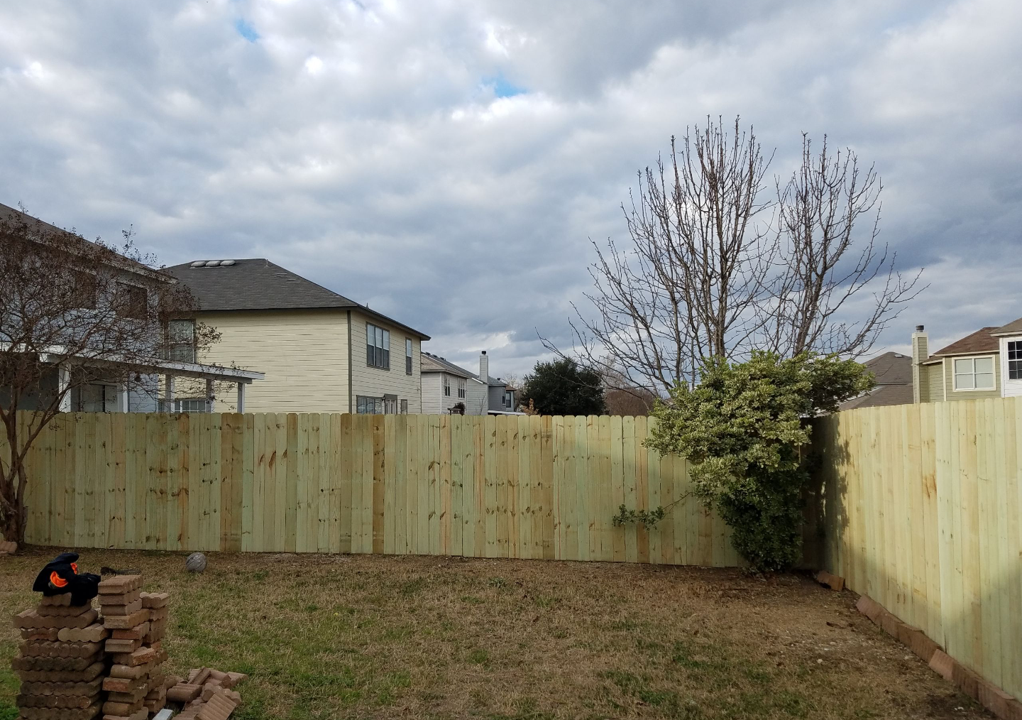 A backyard with a wooden fence and a house in the background